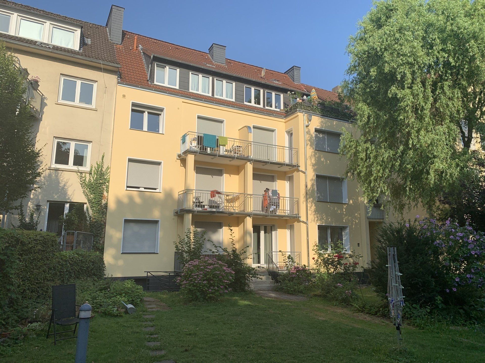 Gelbes Mehrfamilienhaus mit Balkonen und Garten.