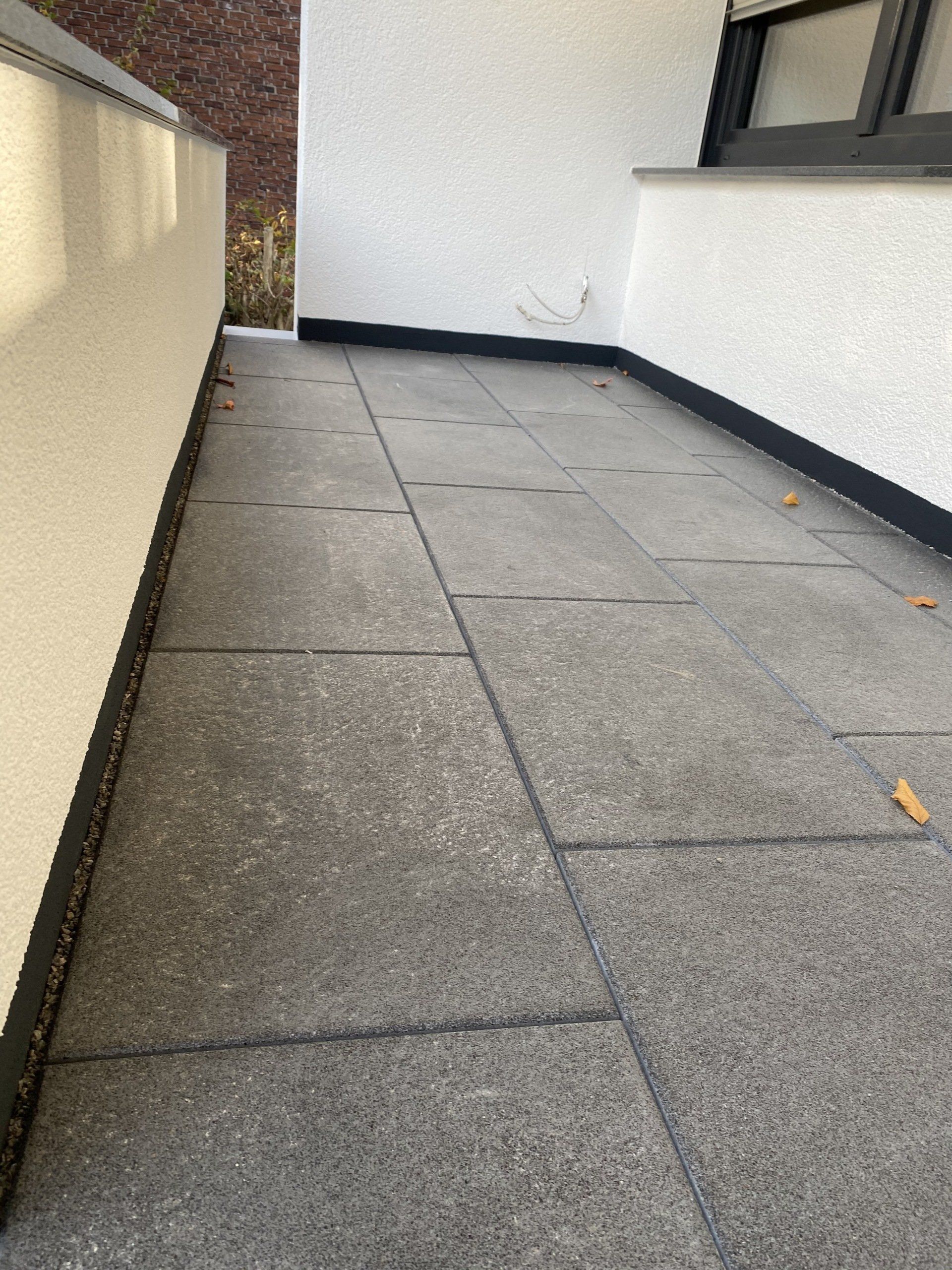 Terrasse aus grauen Steinfliesen mit weißen Wänden und schwarzen Zierleisten.