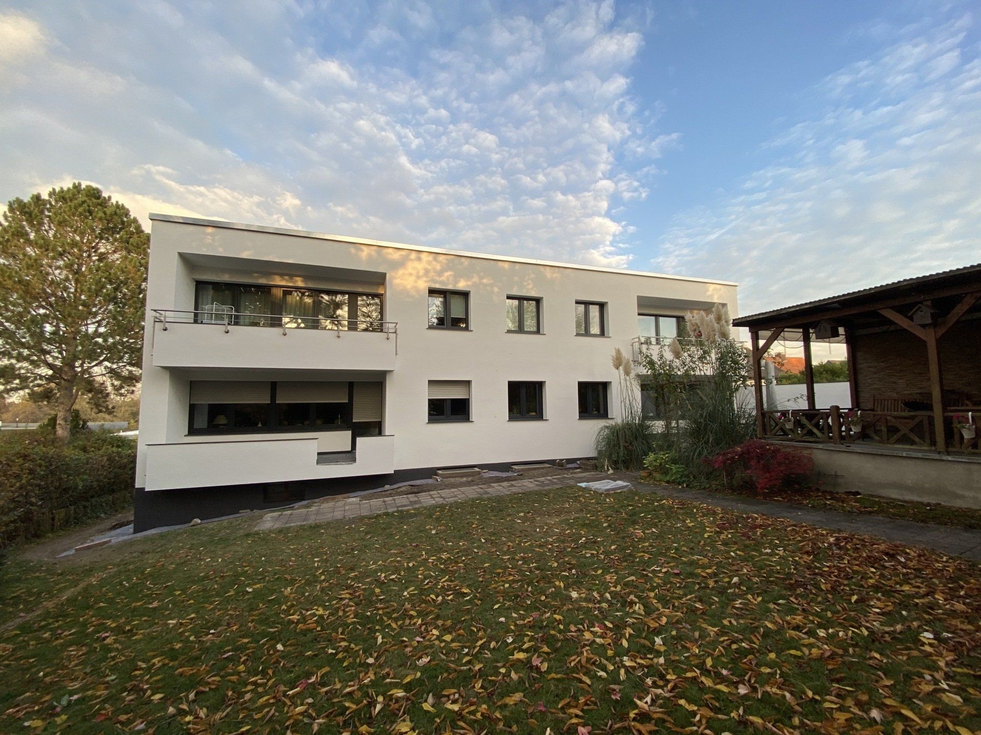 Weißes Gebäude mit dunklen Fenstern und einem Rasen. Sonniger Tag mit blauem Himmel.