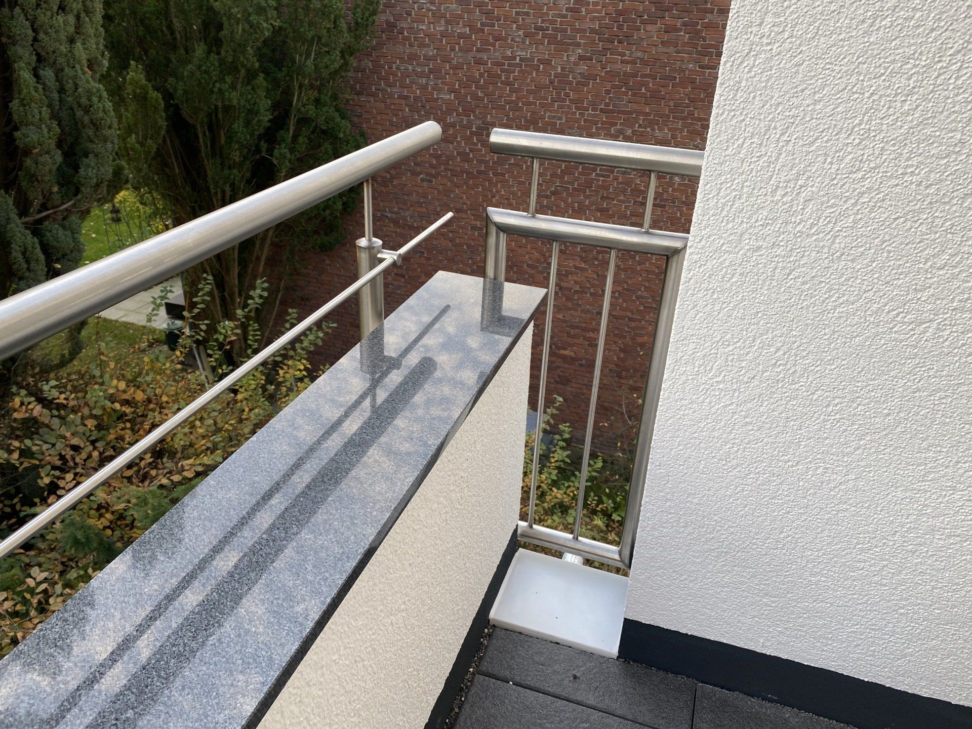 Balkon mit Edelstahlgeländer, Granitsims und weißer strukturierter Wand.