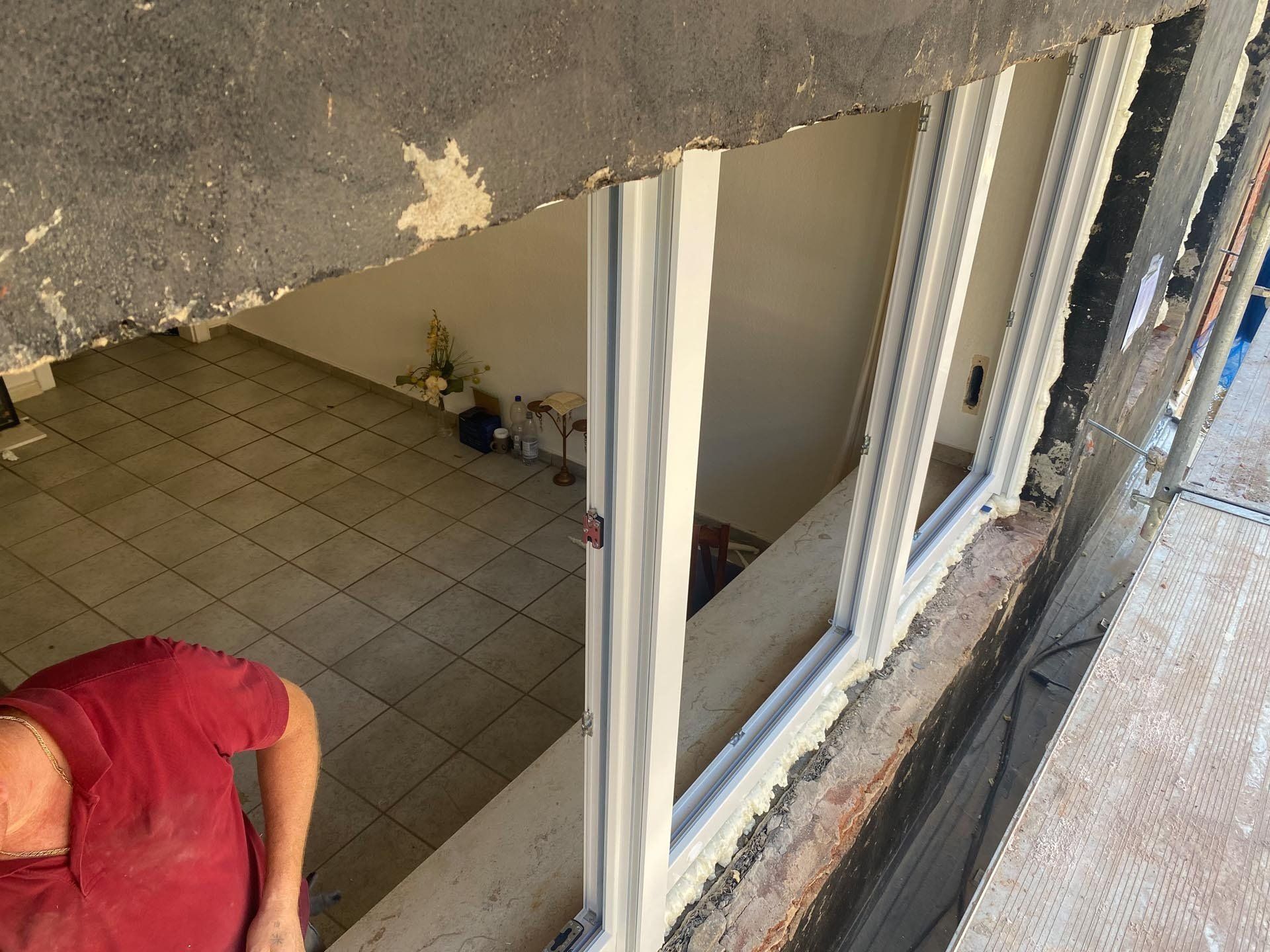 Mann im roten Hemd schaut in einen Fensterrahmen. Innenansicht mit gefliestem Boden. Weiße Fensterverkleidung.