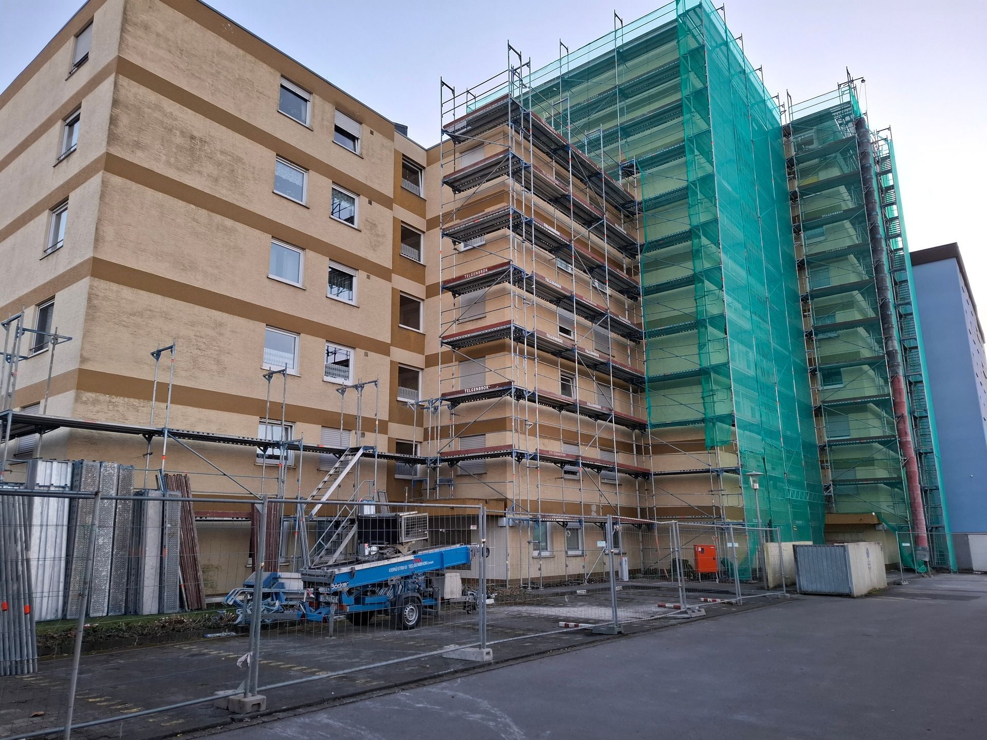 Gebäude im Umbau mit Gerüst und grünem Netz. Beige Ziegelfassade.