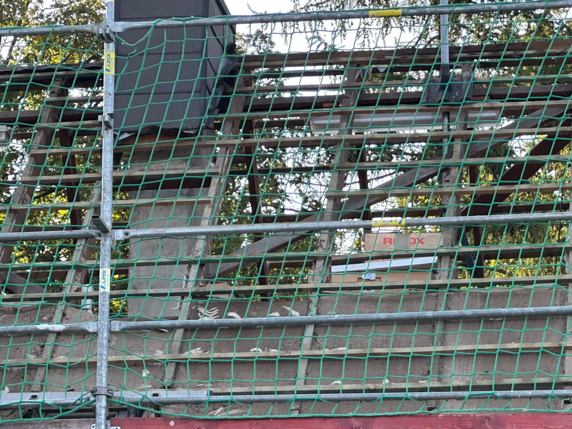 Gerüst mit grünem Sicherheitsnetz an einer freiliegenden Gebäudestruktur, möglicherweise im Bau.