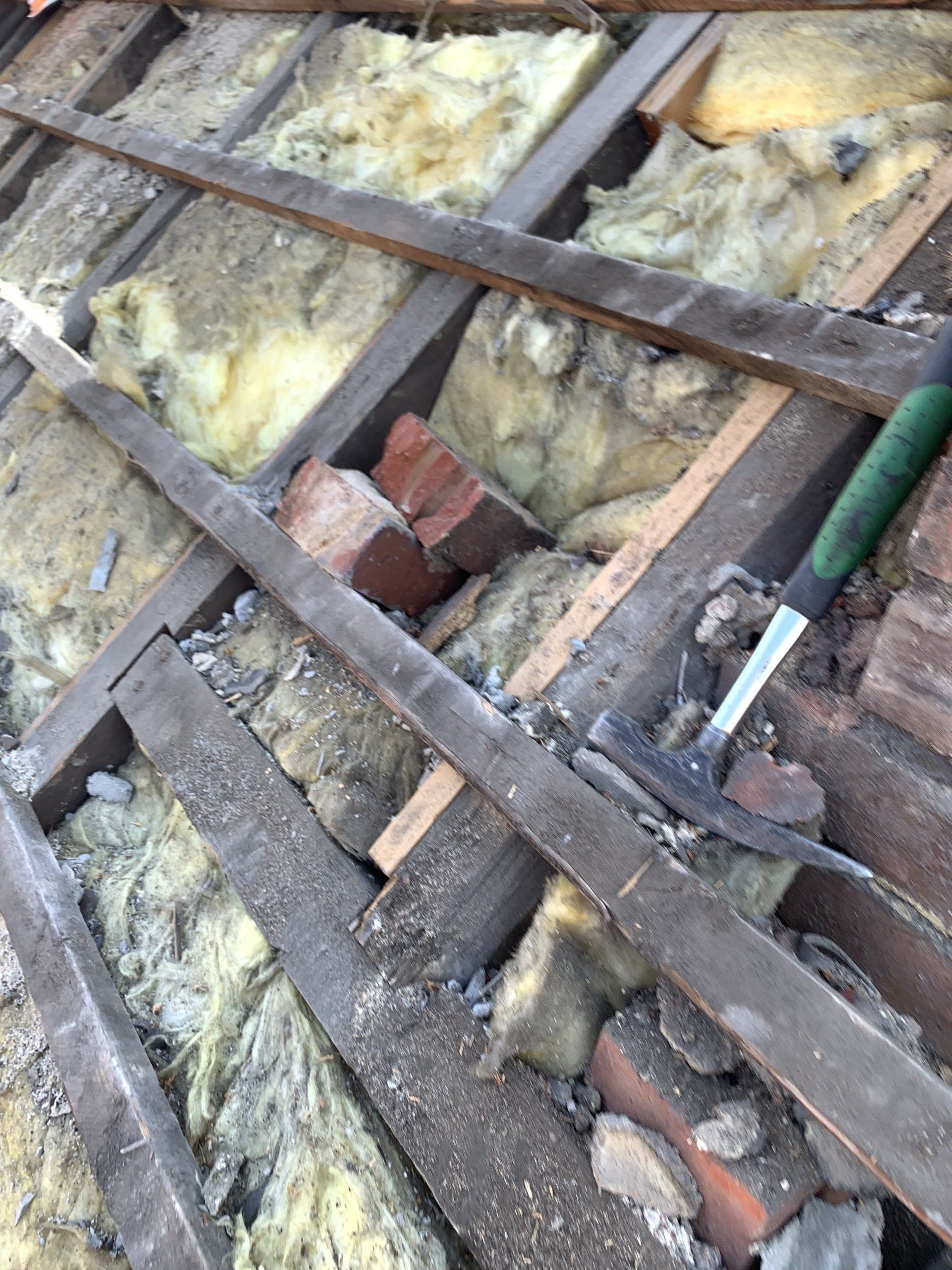 Im Inneren eine Dachkonstruktion mit Isolierung, Holzbalken, Ziegeln und einem Hammer.