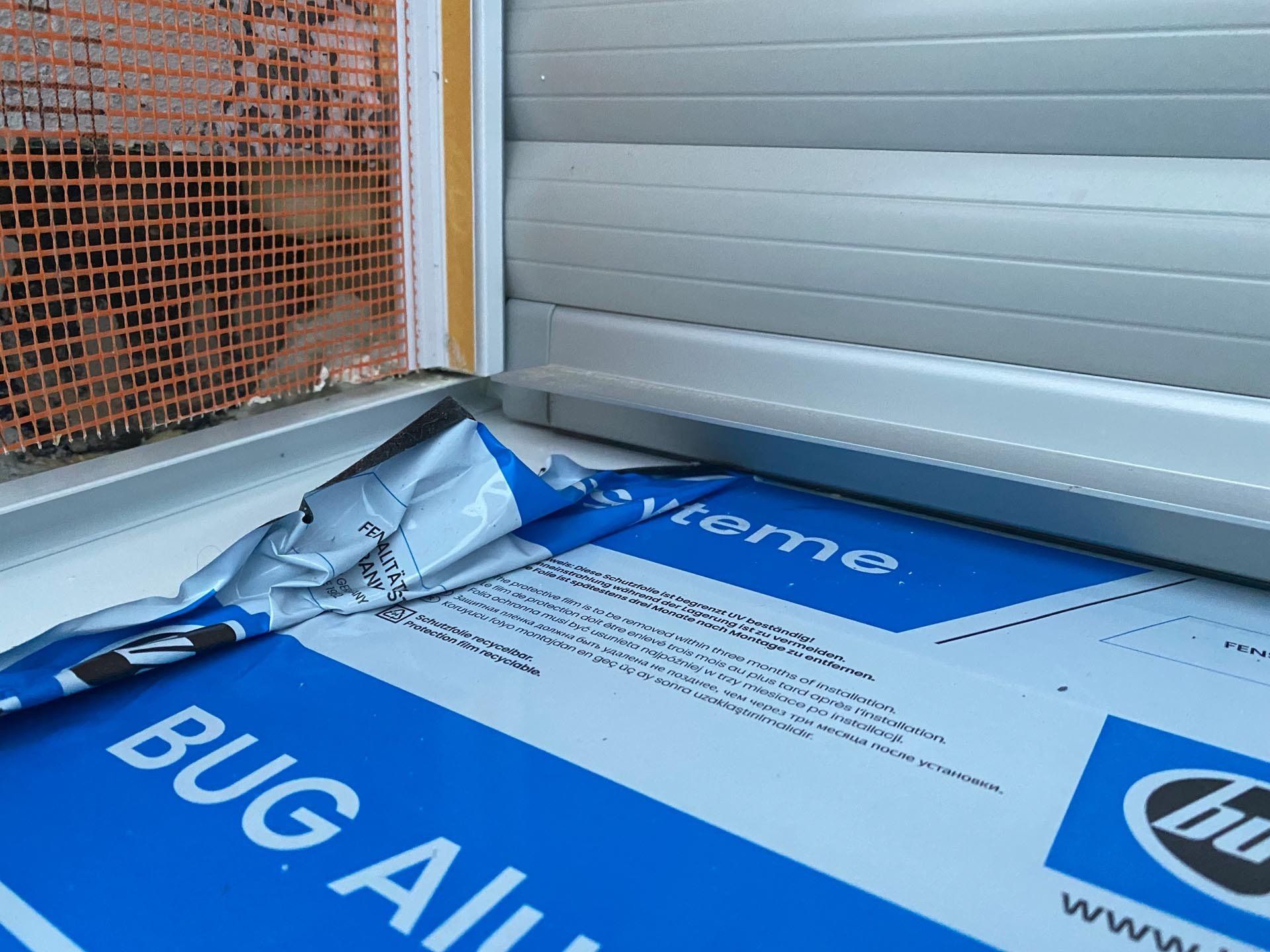 Nahaufnahme einer Fensterinstallation. Blaue und silberne Bug-Alaun-Folie, Ziegelwand und silberne Fensterläden.