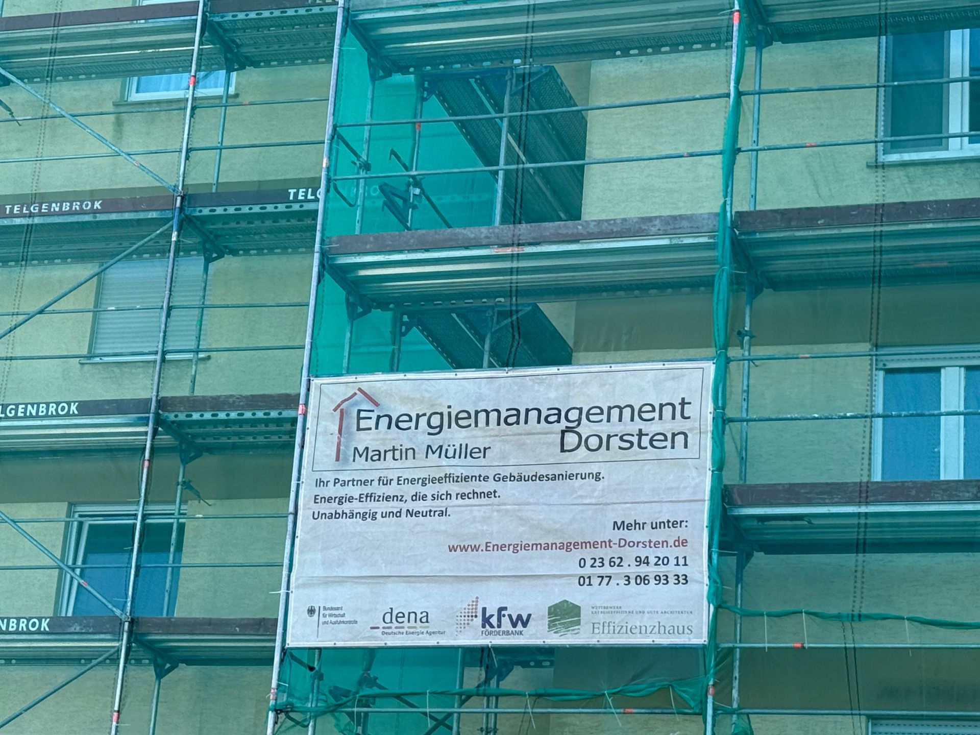Gebäudefassade mit Gerüst, grünem Netz und Schild „Energiemanagement Dursten“.
