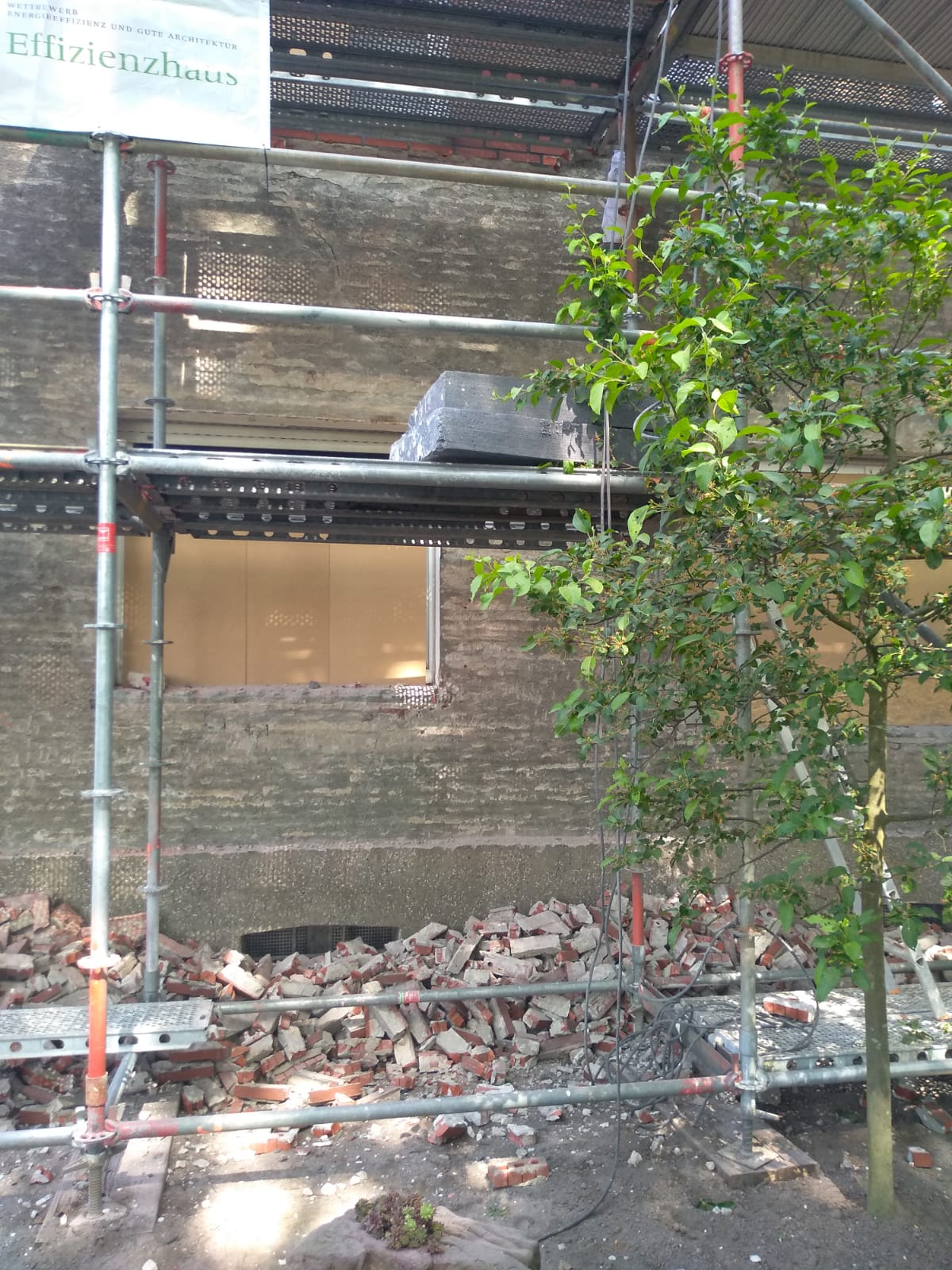 Im Bau befindliches Backsteingebäude mit Gerüst, Schutt und einem kleinen Baum.