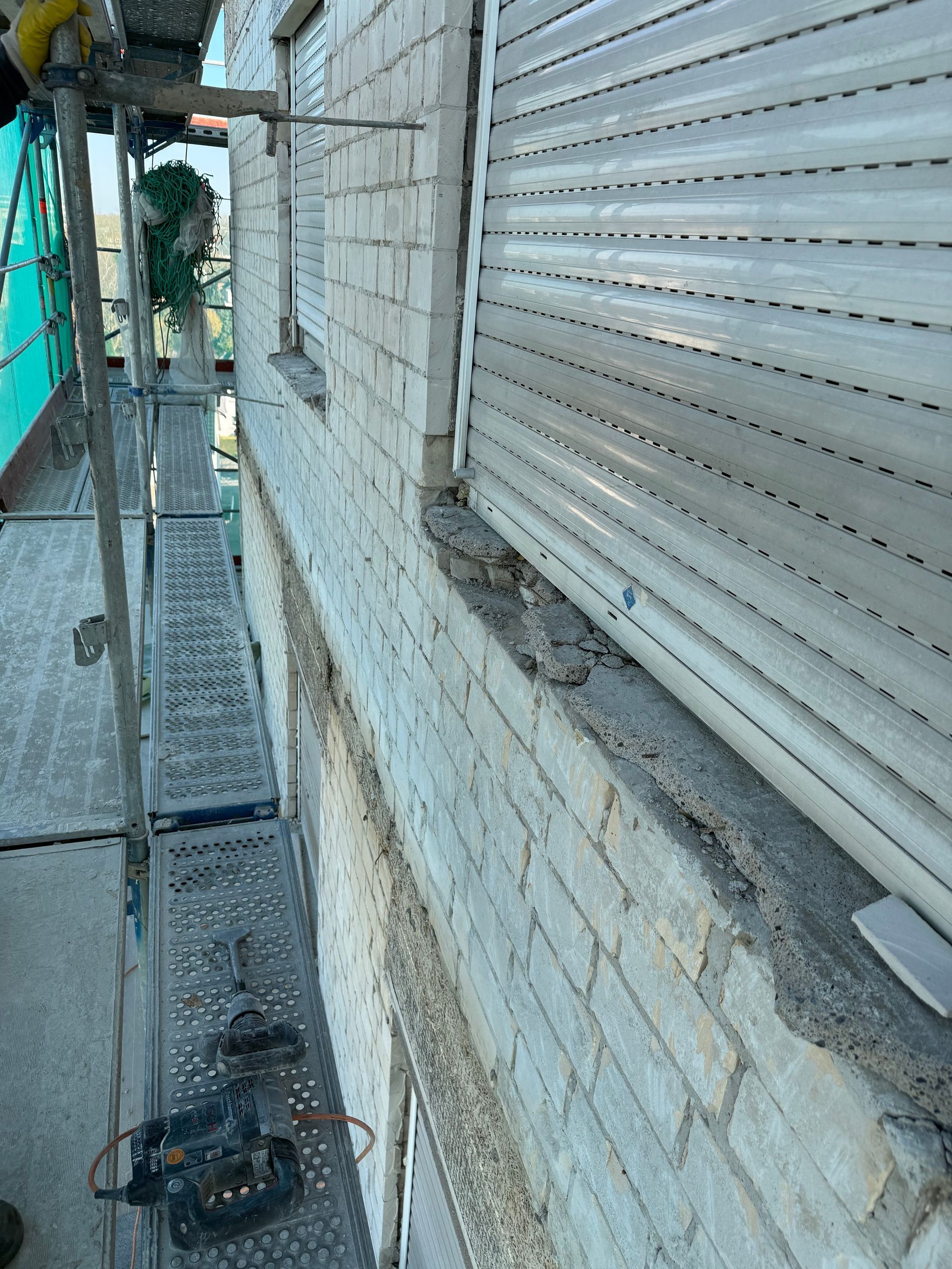 Außenansicht eines Backsteingebäudes mit Gerüst. Fenster mit geschlossenen weißen Fensterläden.