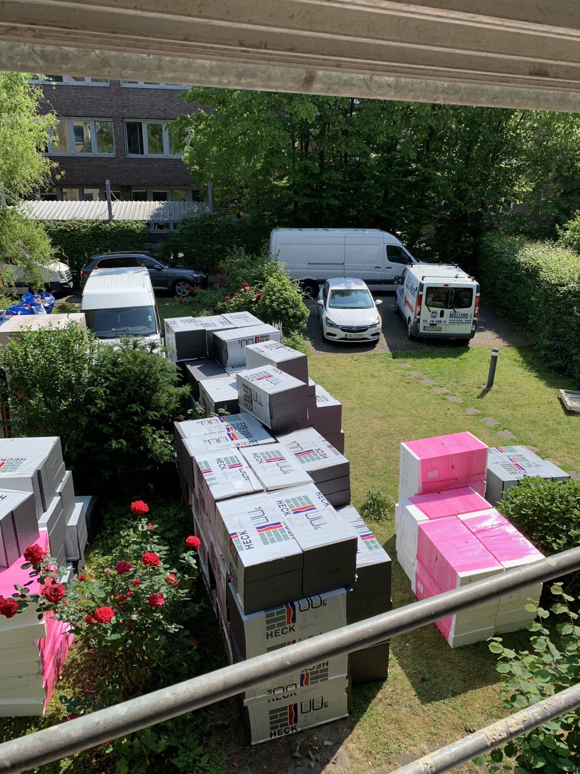 Auf grünem Gras gestapelte Isolierkartons, im Hintergrund Fahrzeuge und Gebäude.