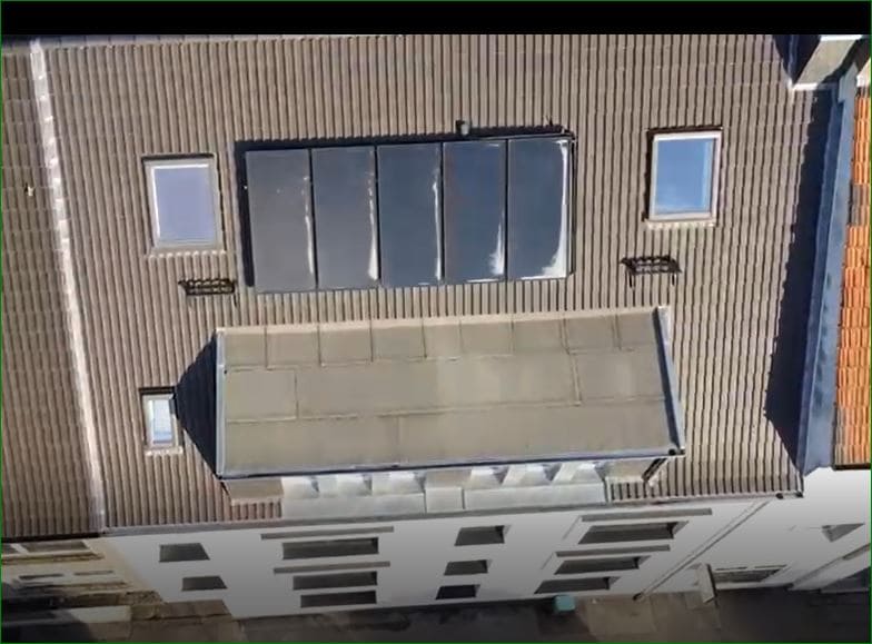 Draufsicht auf ein Gebäude mit Solarmodulen auf dem Dach und mehreren Fenstern.