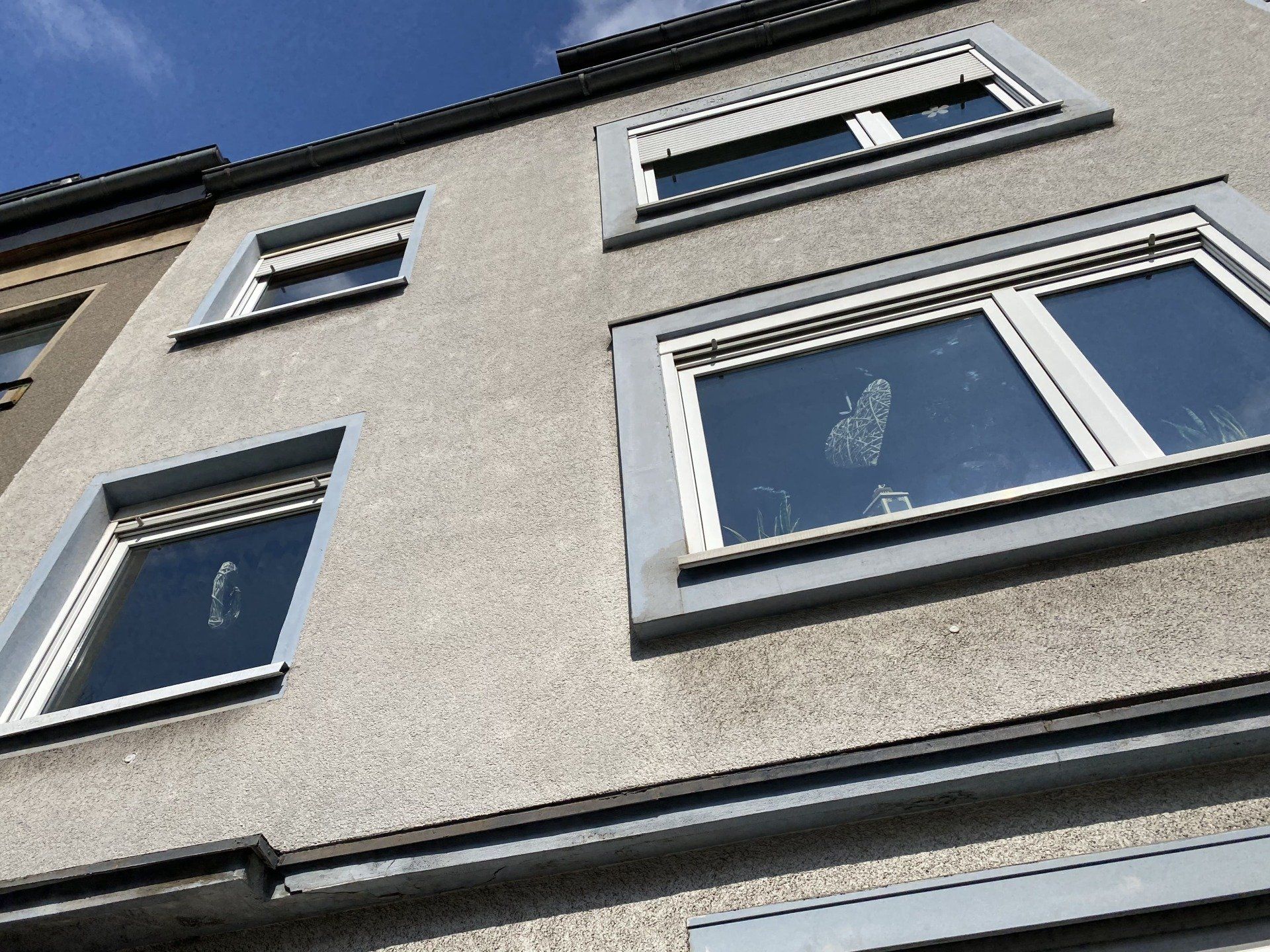 Untersicht einer grauen Gebäudefassade mit Fenstern. Darüber ist der Himmel sichtbar.