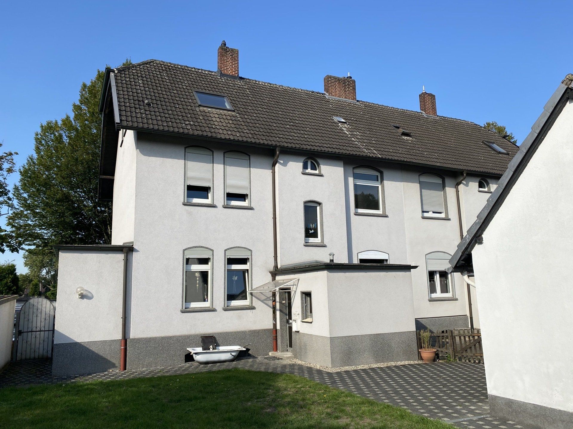 Zweistöckiges weißes Gebäude mit dunklem Dach und grauen Zierleisten, Hinterhof, blauer Himmel.
