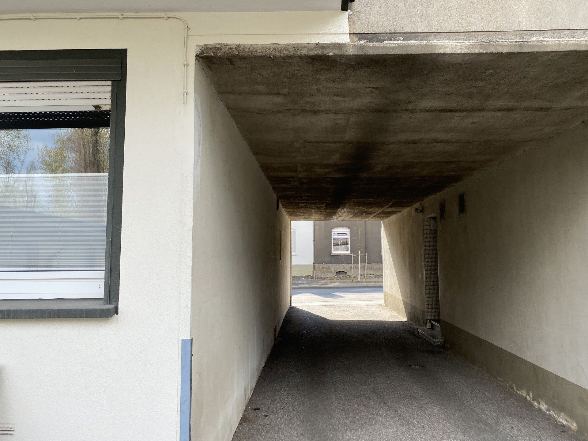 Ein tunnelartiger Durchgang mit Licht am Ende, eingerahmt von weißen Wänden und einer Betondecke.