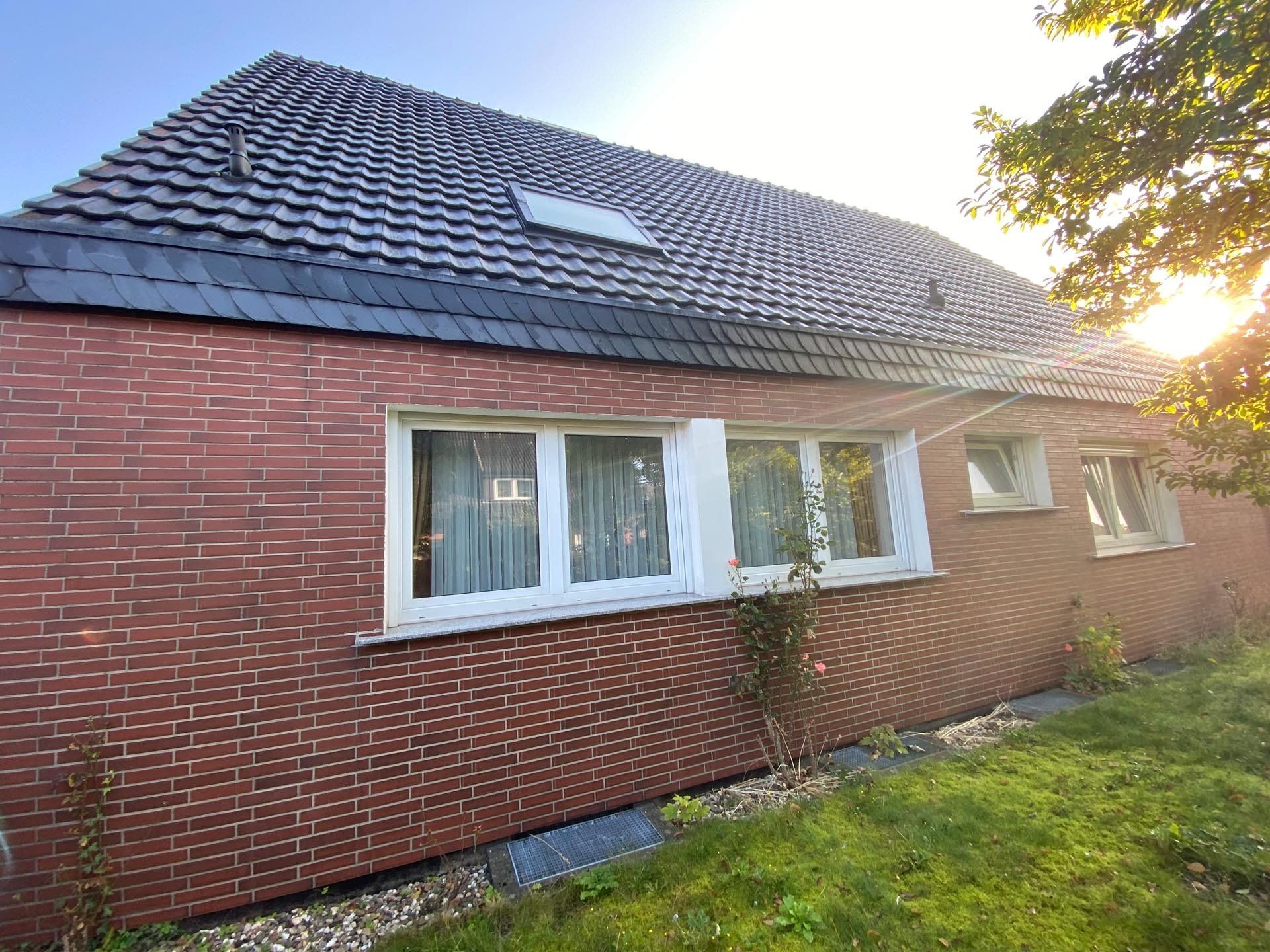 Rotes Backsteinhaus mit grauem Ziegeldach, weiß gerahmten Fenstern und Rasenfläche.