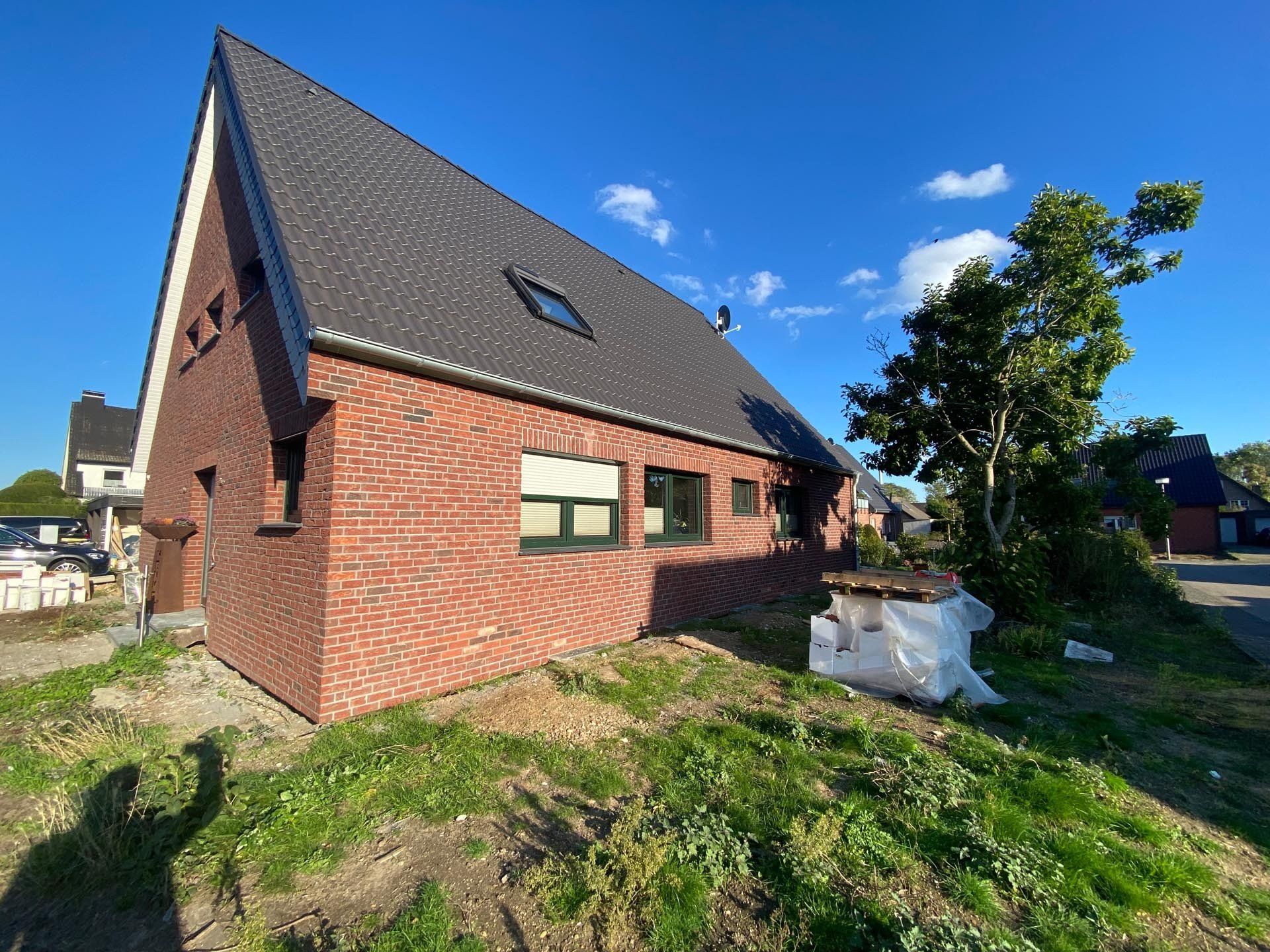 Rotes Backsteinhaus mit dunkelgrauem Dach unter blauem Himmel. Das Haus hat Fenster und ein schräges Dach.