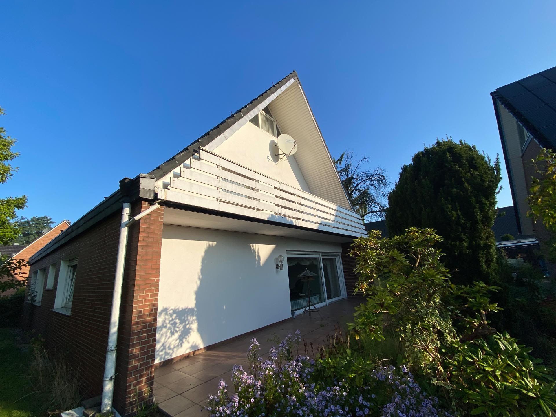 Haus mit weißem dreieckigem Balkon, Ziegel- und weißen Wänden, blauer Himmel.
