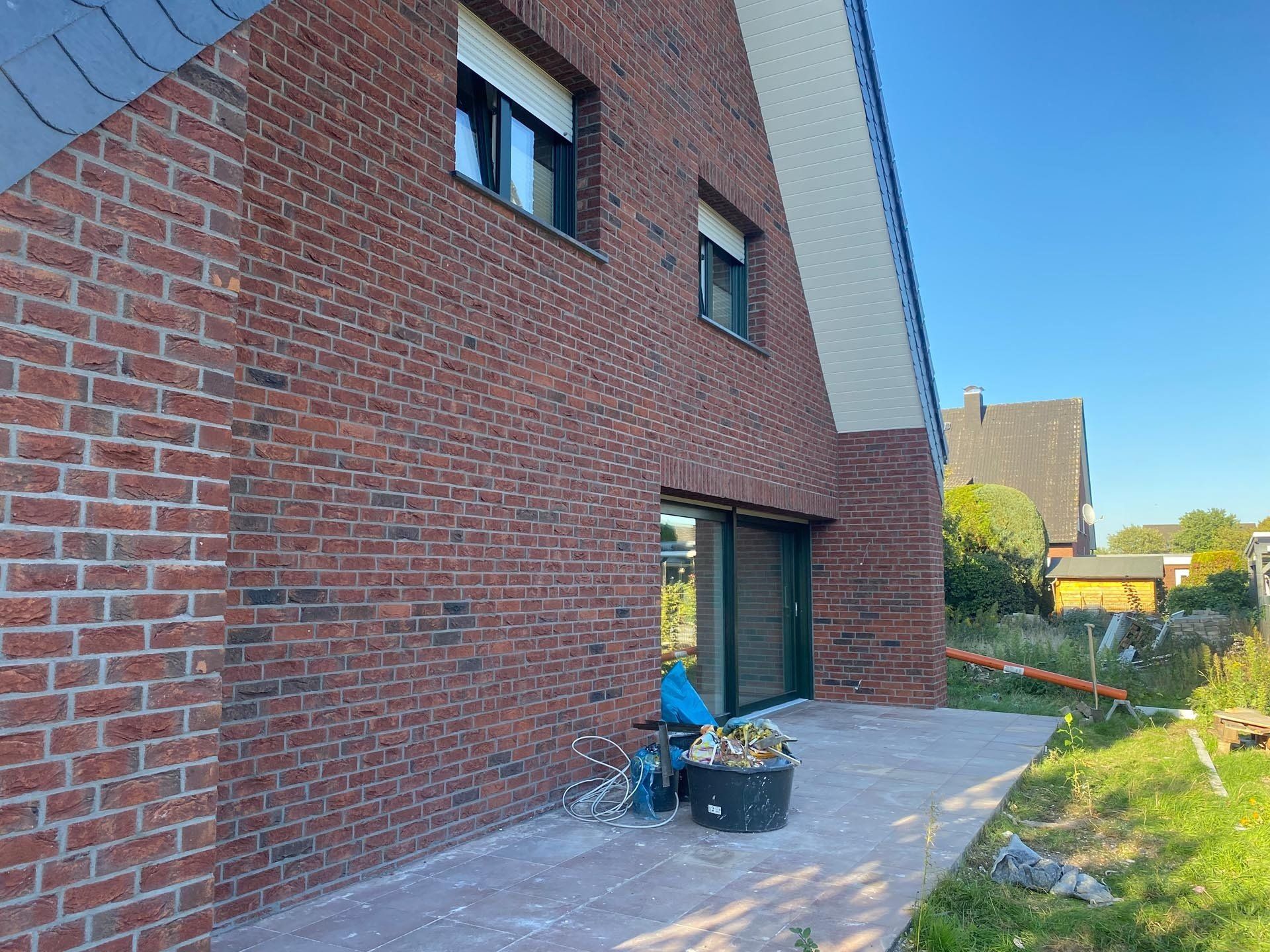 Außenansicht eines Backsteinhauses mit Glasschiebetür, Terrasse und Garten.