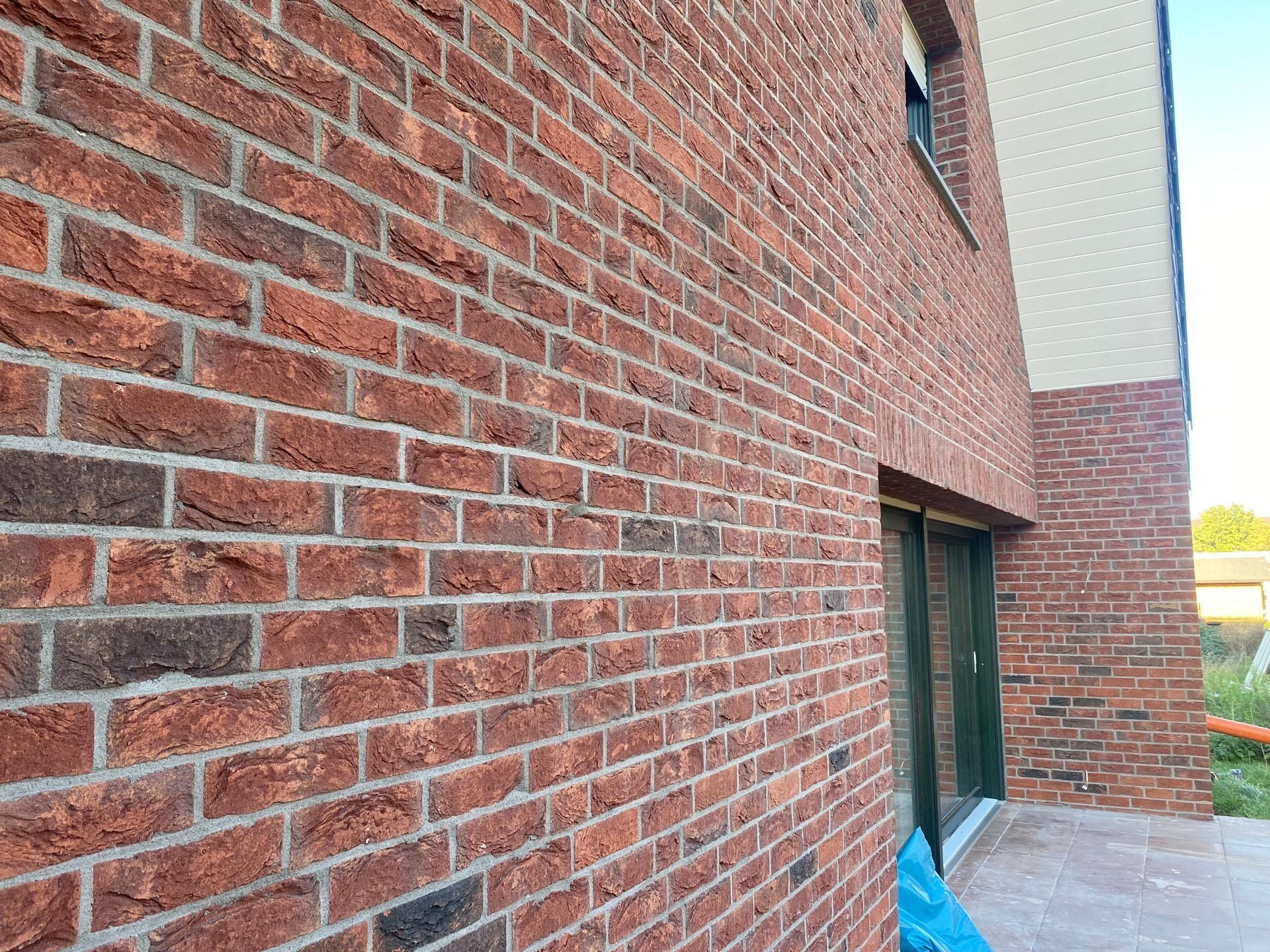 Außenwand eines Gebäudes aus rotem Backstein mit einer Glasschiebetür und einem Blick auf das Dach.