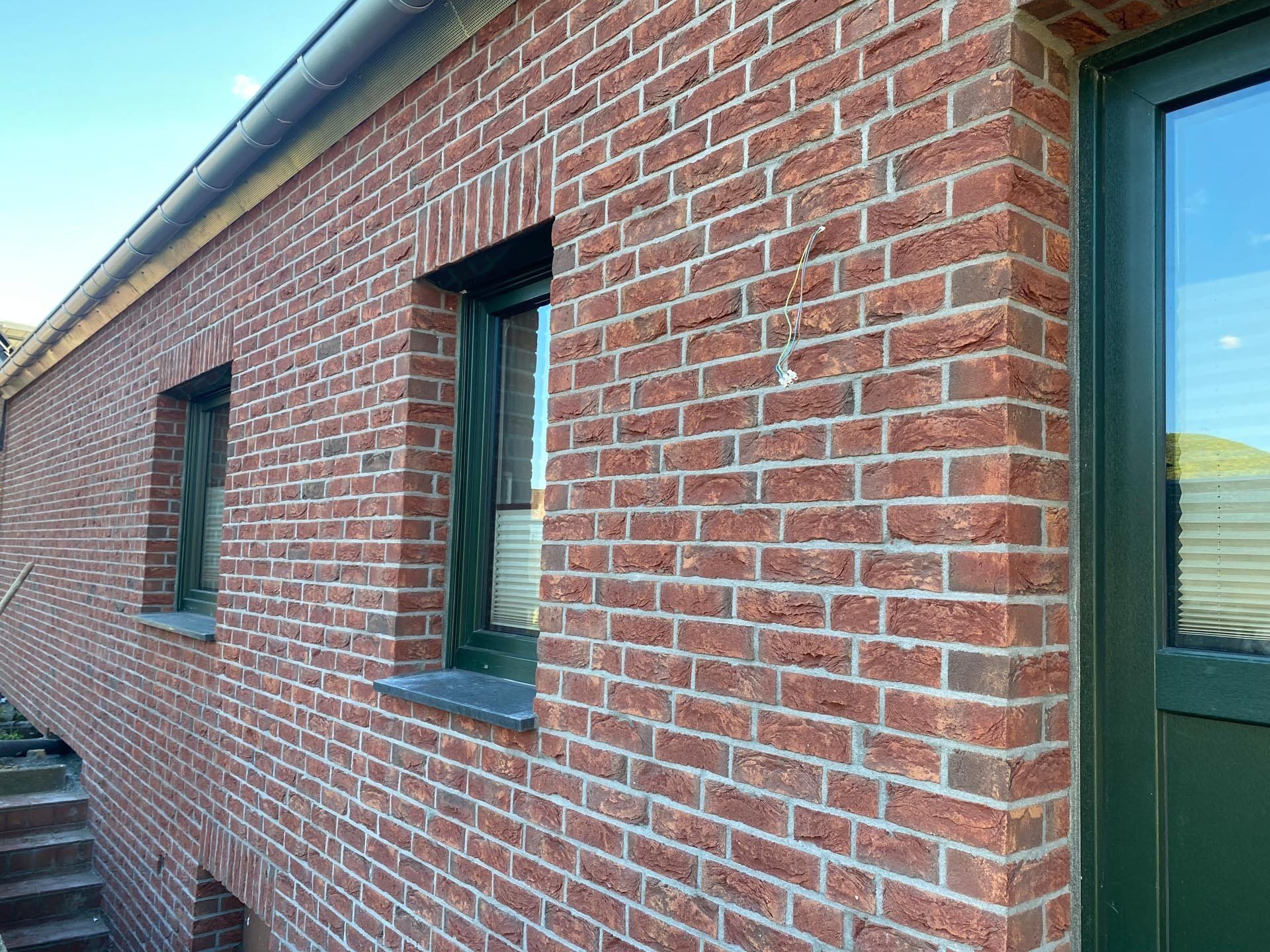 Rotes Backsteingebäude mit grün gerahmten Fenstern und Türen.