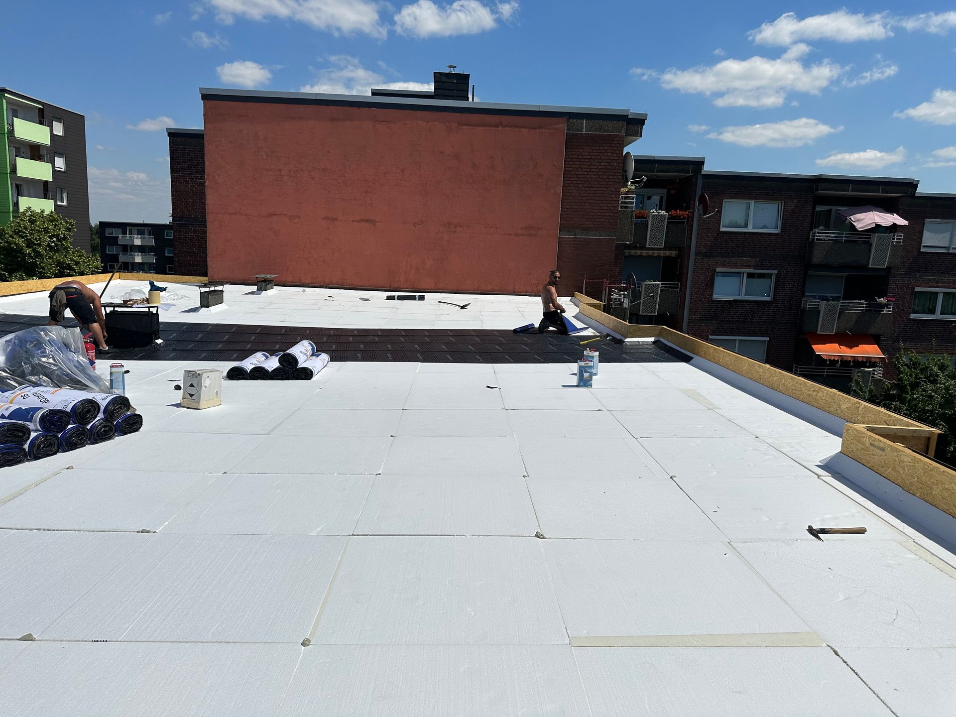 Arbeiter installieren unter blauem Himmel eine weiße Dachisolierung auf dem Dach eines Stadtgebäudes.