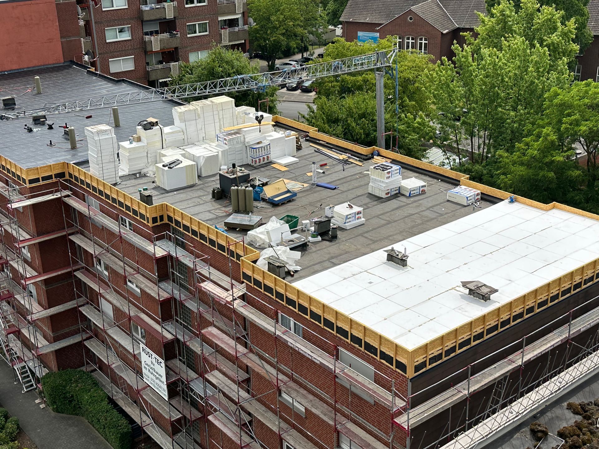 Gebäudedach im Bau; Ziegel, Gerüst, Isolierung, Kran und Ausrüstung sichtbar.