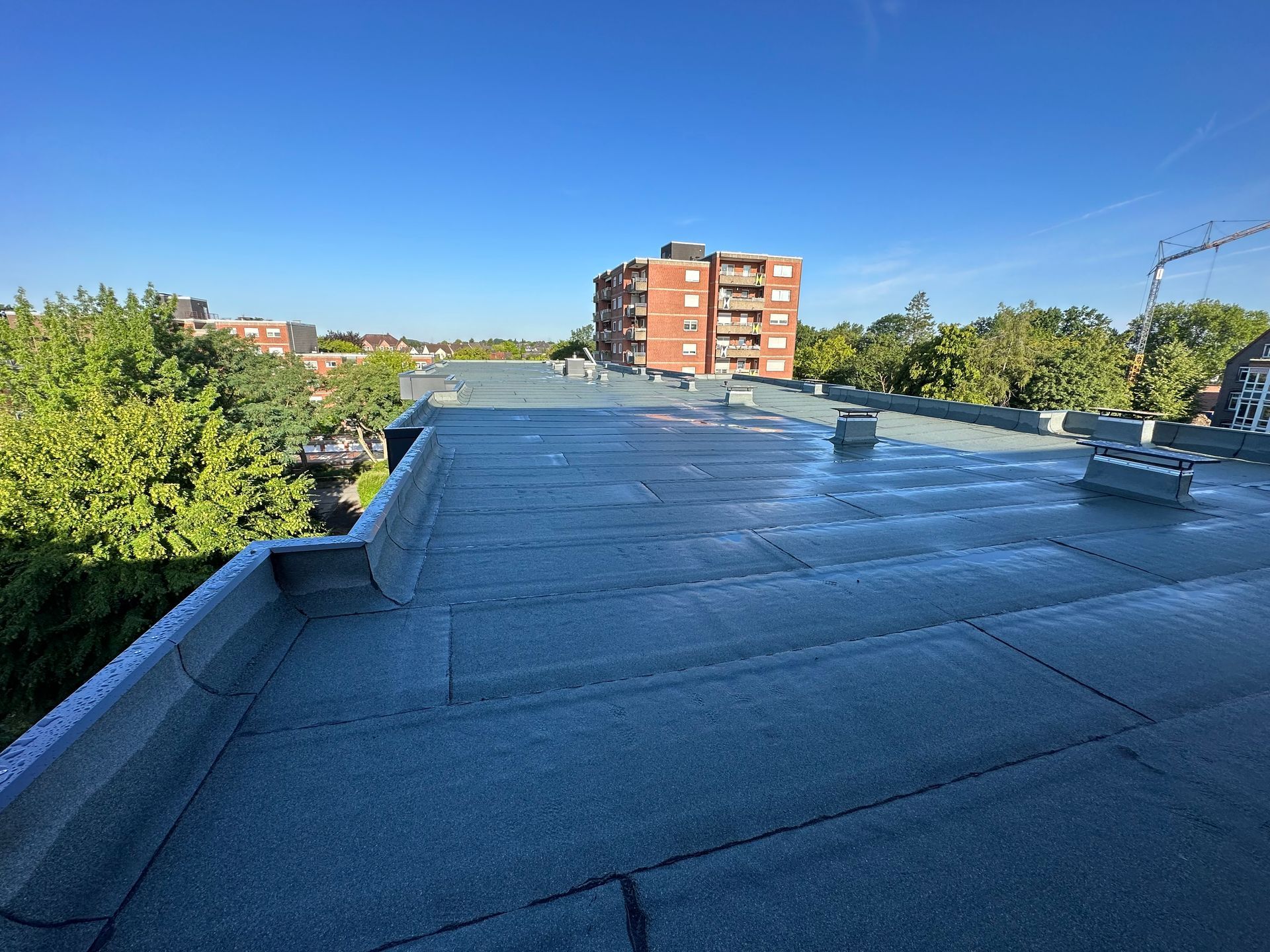 Flaches, blaugraues Dach mit der Skyline einer Stadt im Hintergrund unter einem klaren, blauen Himmel.