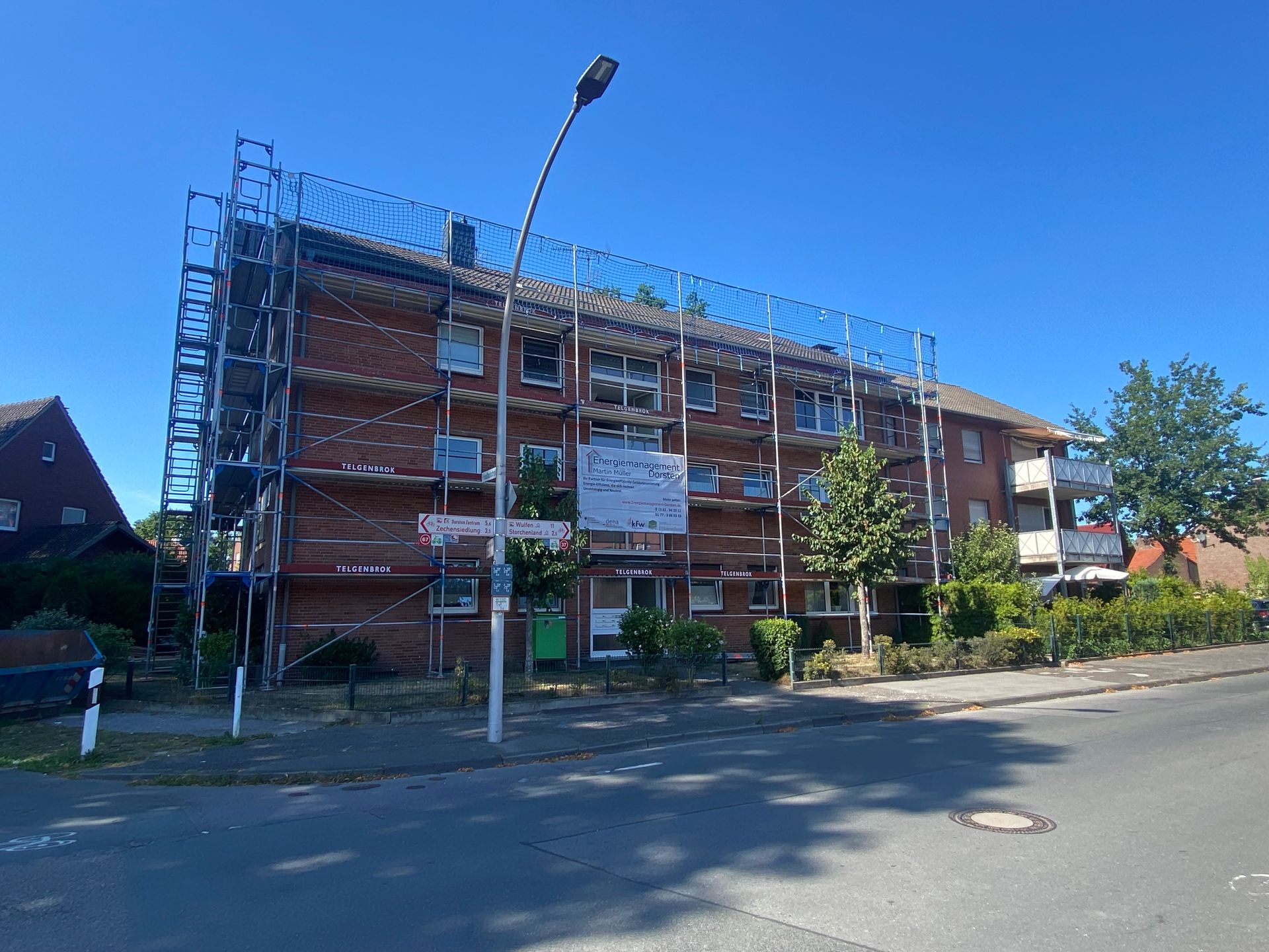 Gebäude mit Gerüst, rotem Backstein, Straße, blauer Himmel.