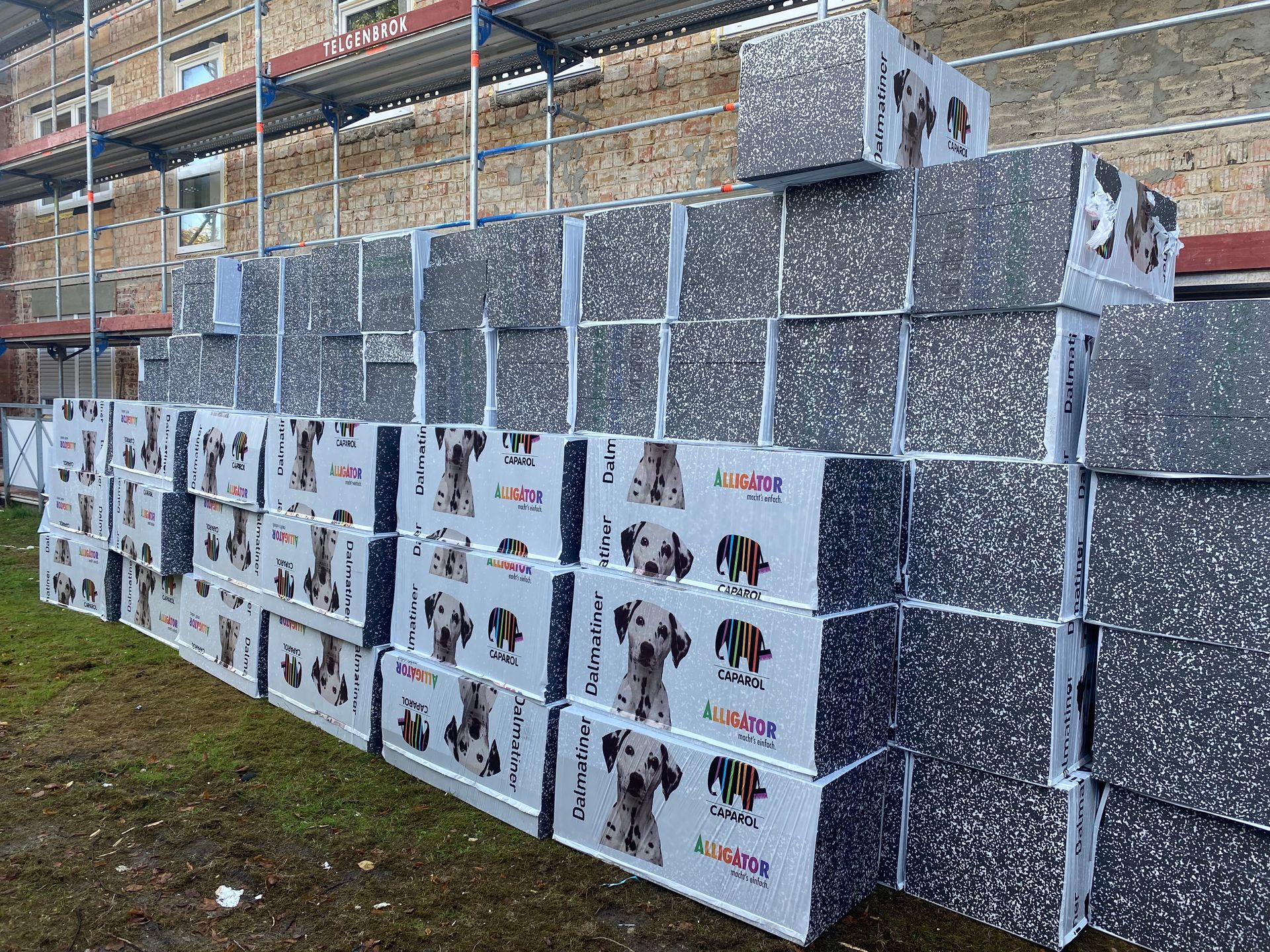 Stapel von Dämmblöcken mit Dalmatiner-Hundemotiv neben einem Backsteingebäude unter einem Gerüst.