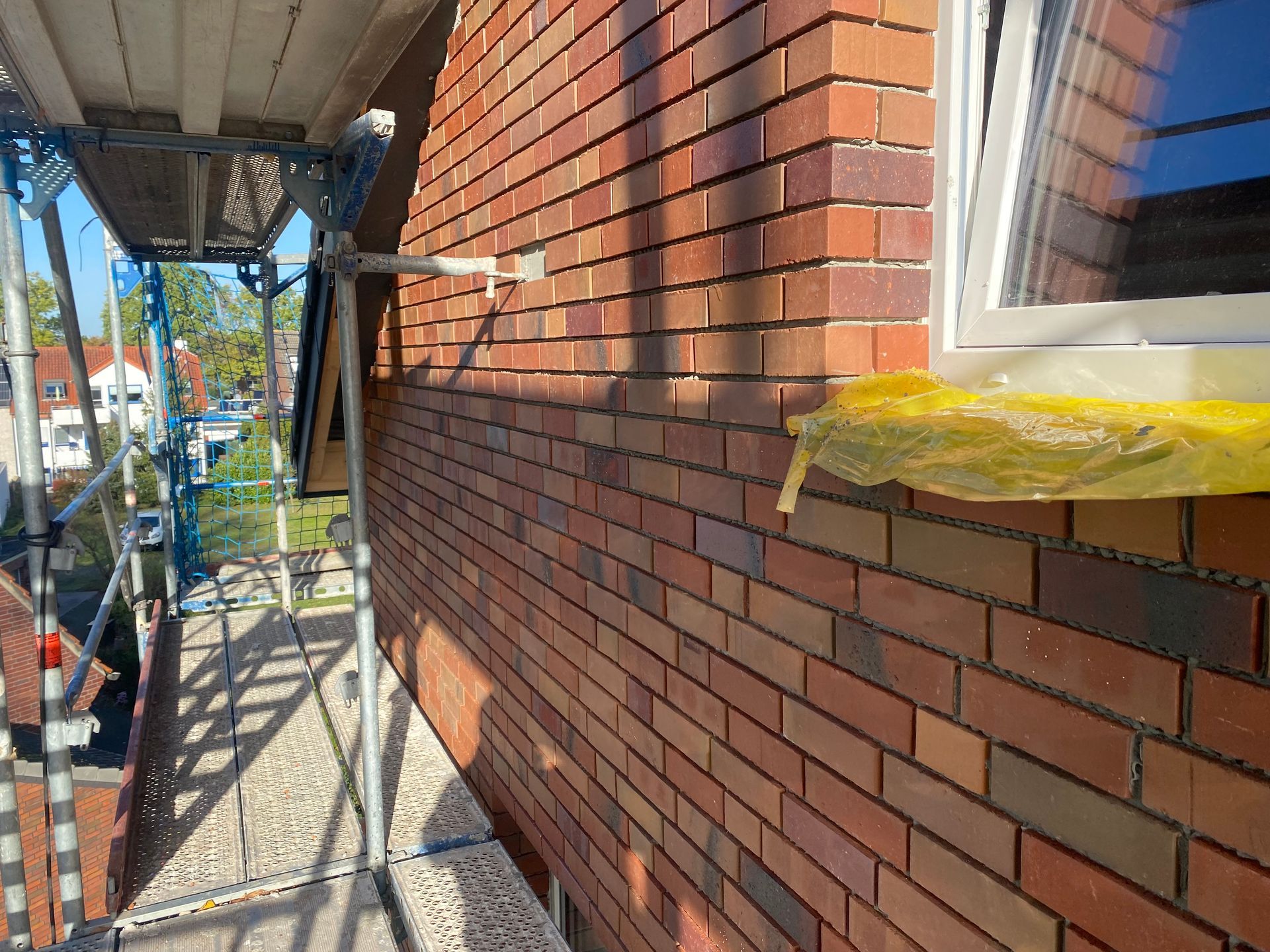 Neben einem Fenster wird mit Gerüst eine Ziegelmauer errichtet.