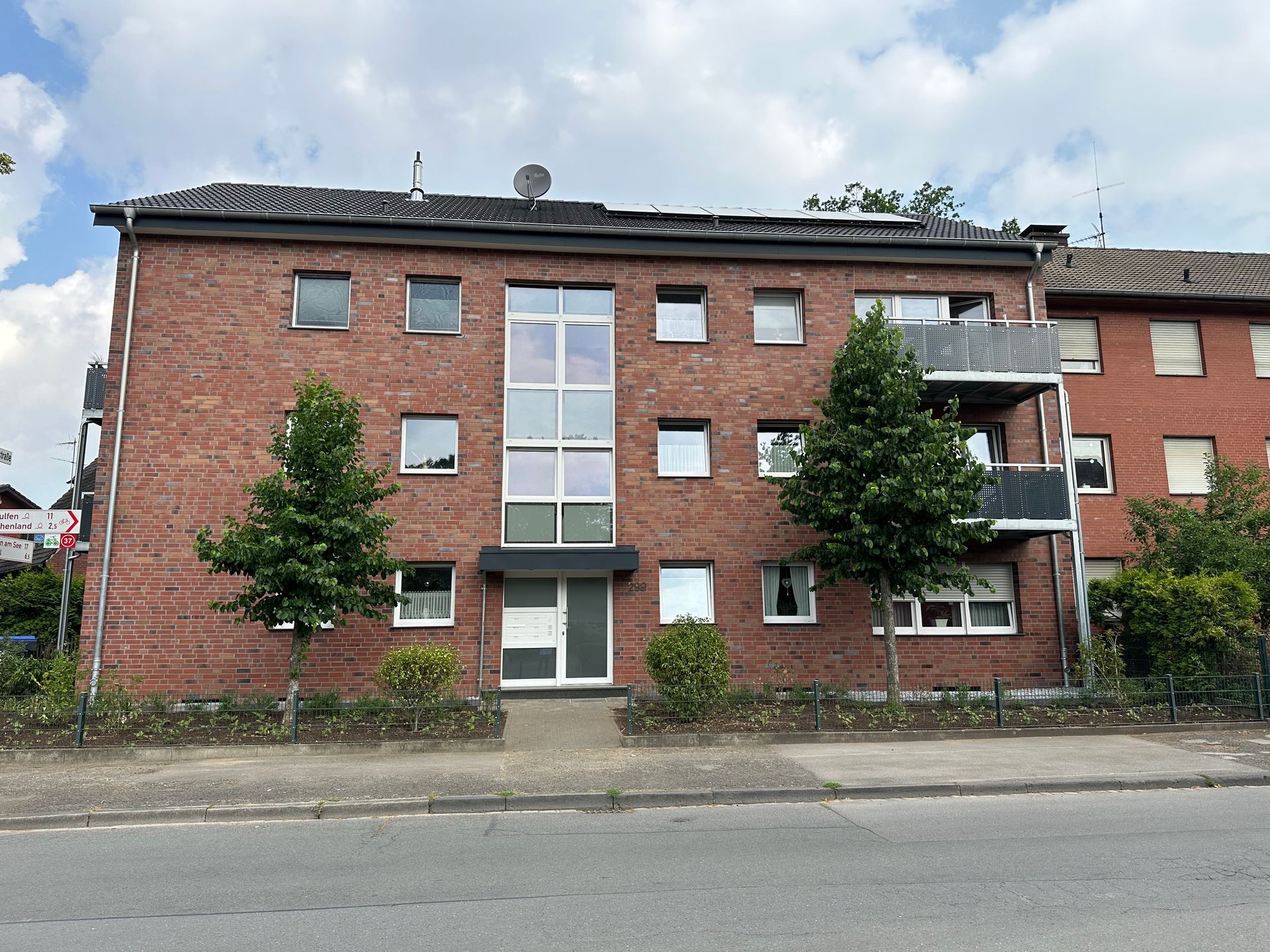 Backstein-Wohnhaus mit mehreren Fenstern, Bäumen und einem grauen Dach.