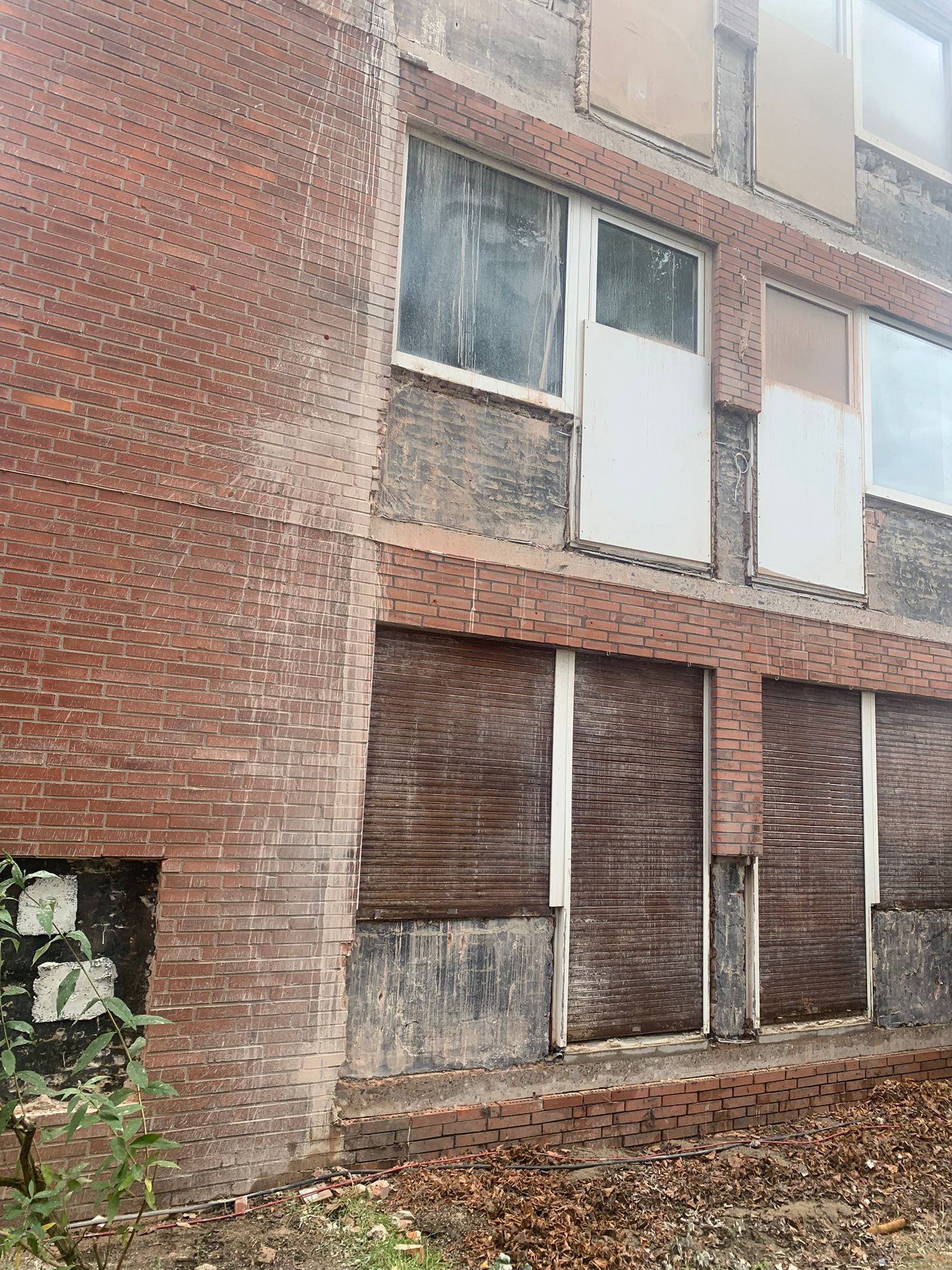 Backsteingebäude mit vernagelten Fenstern. Verfallene Fassade; Blätter auf dem Boden.