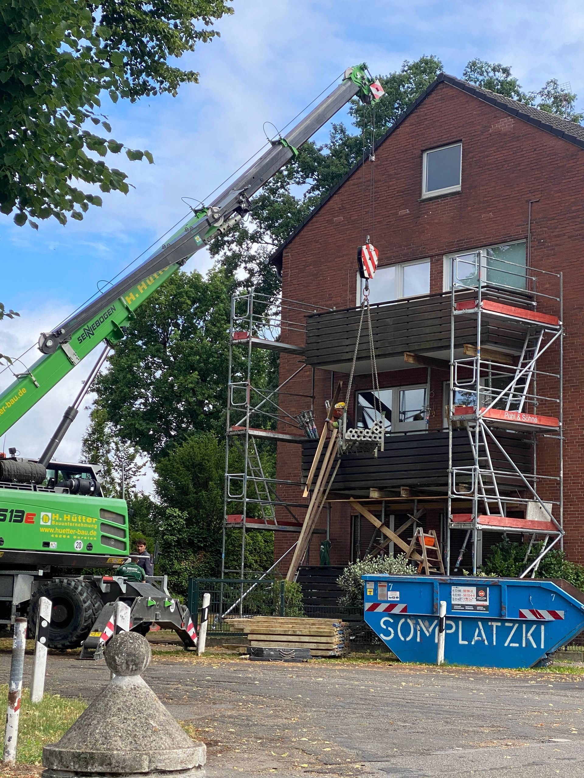 Baustelle: grüner Kran, Gerüst, Backsteinhaus, blauer Müllcontainer mit der Aufschrift „Somplatzki“.
