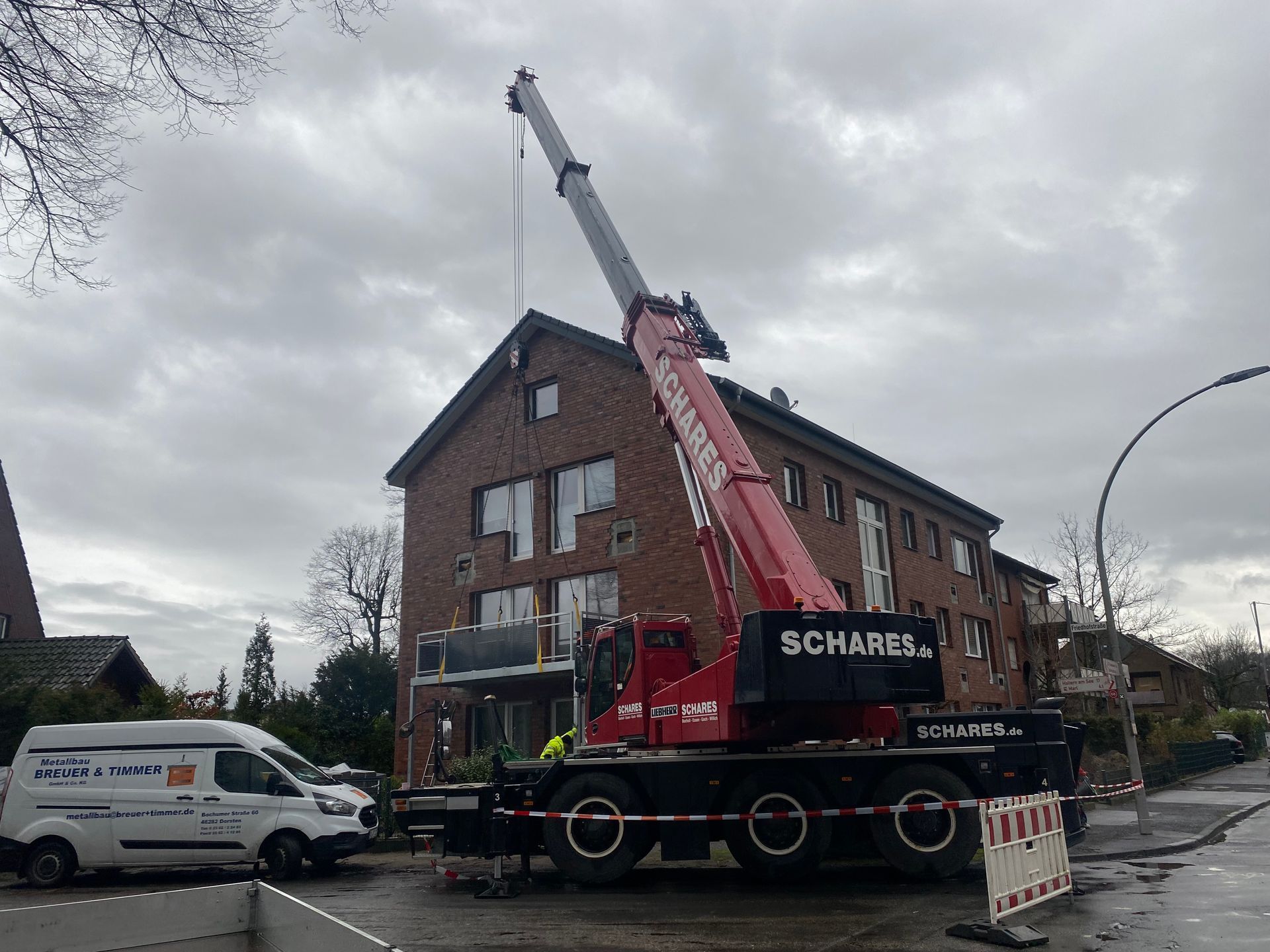 Ein roter Kran hebt unter einem bewölkten Himmel etwas auf ein Backsteingebäude.