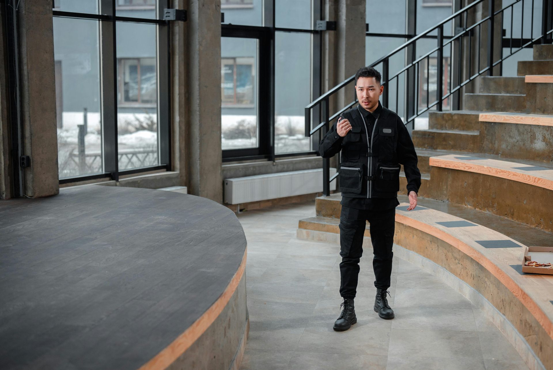 A man in a black jacket is standing in a room with stairs.