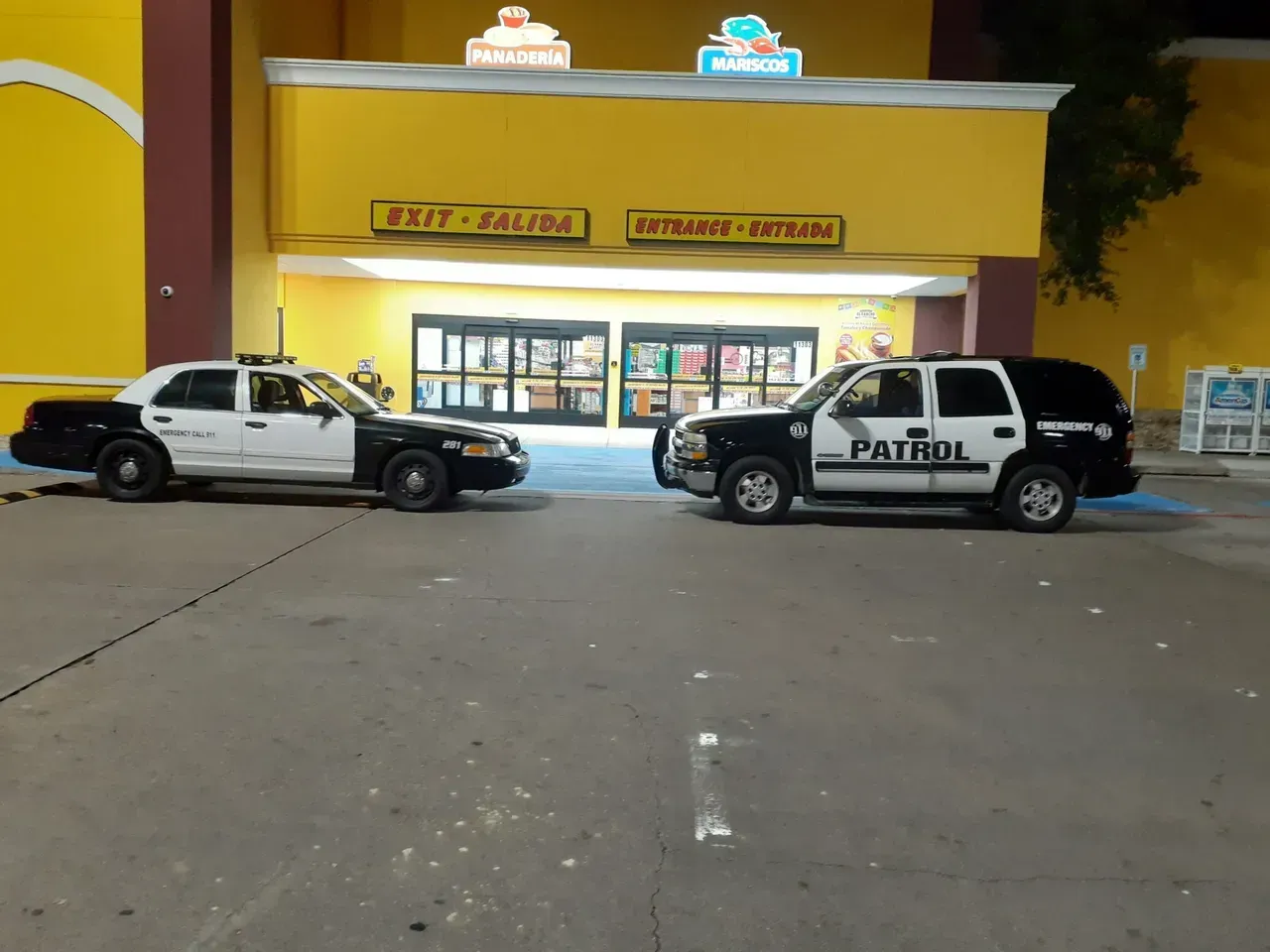 Two patrol cars are parked in front of a yellow building