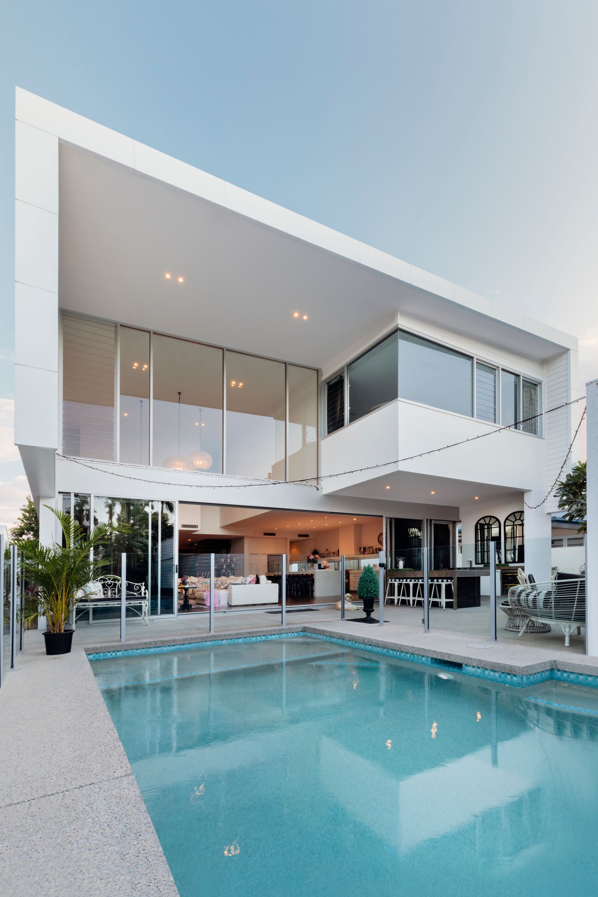 Modern white house with pool; large glass windows, outdoor kitchen, sunny day.
