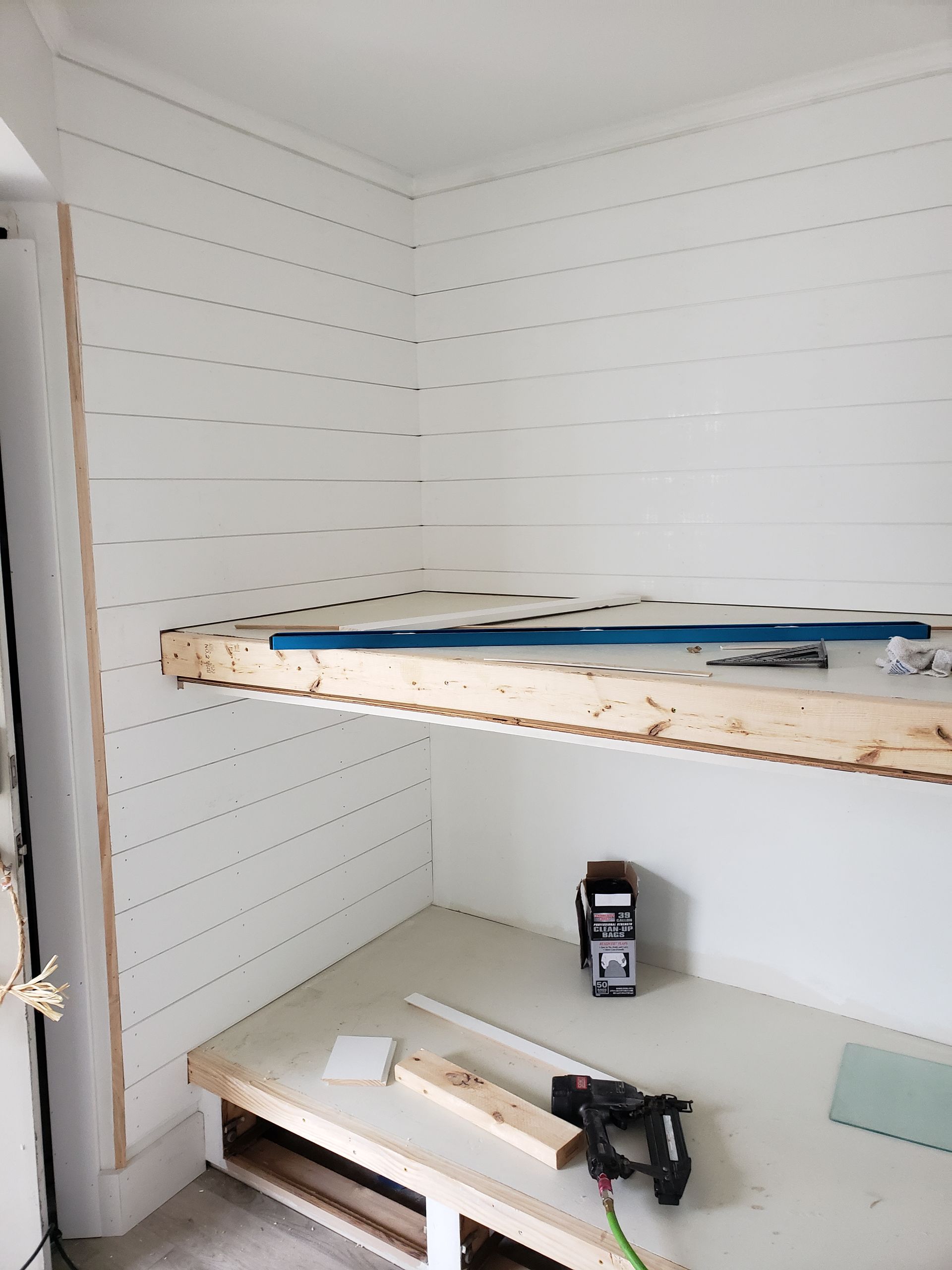 Interior with shiplap walls, wood shelving, and construction tools. White and beige tones.