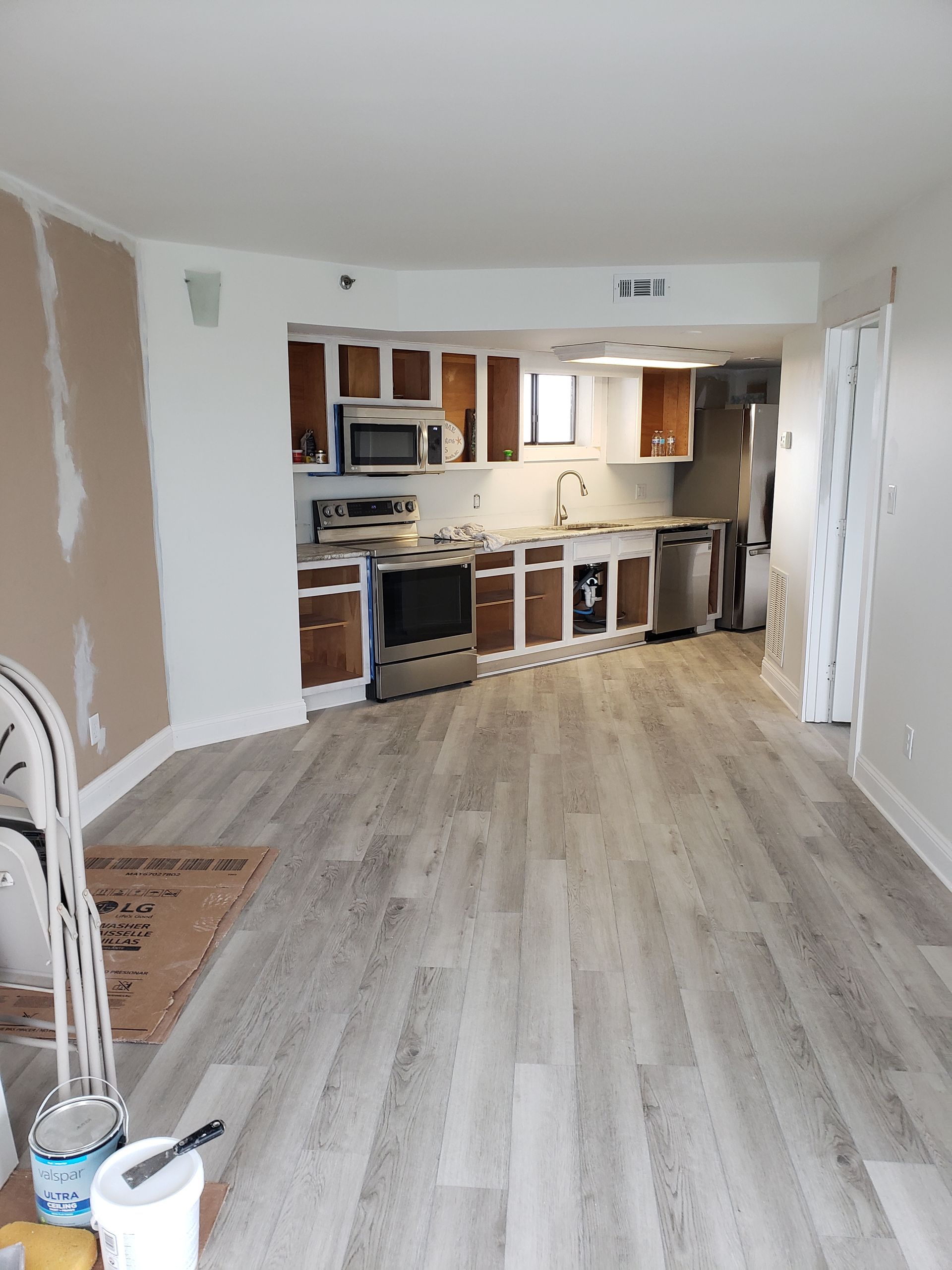 Renovated apartment interior with new flooring and partially painted walls. Kitchen visible.