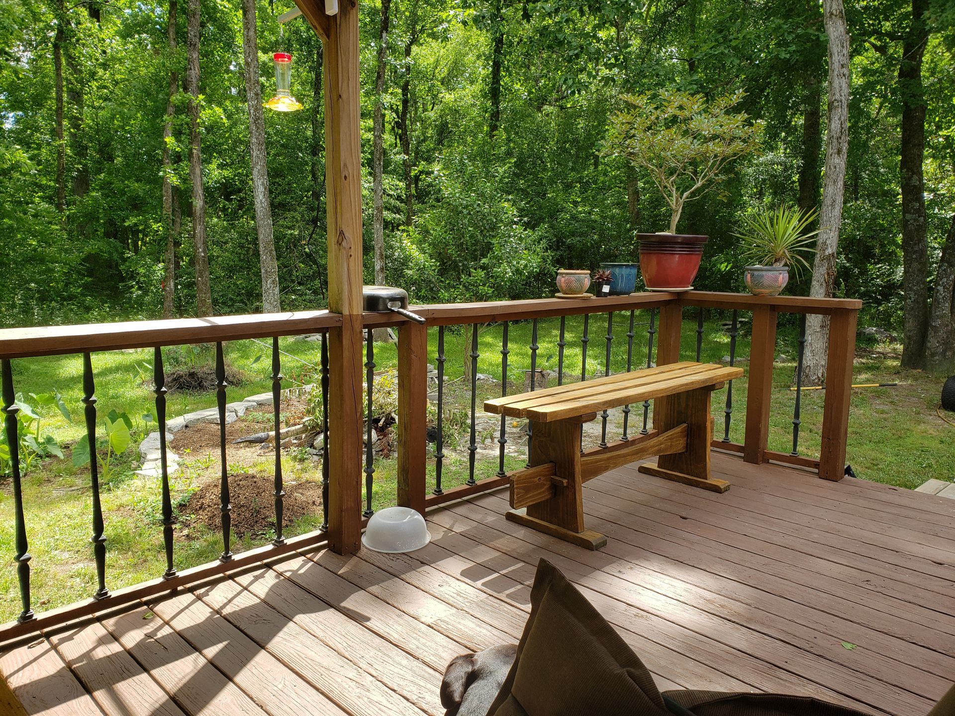 Wooden deck with a bench and potted plants, overlooking a wooded area.