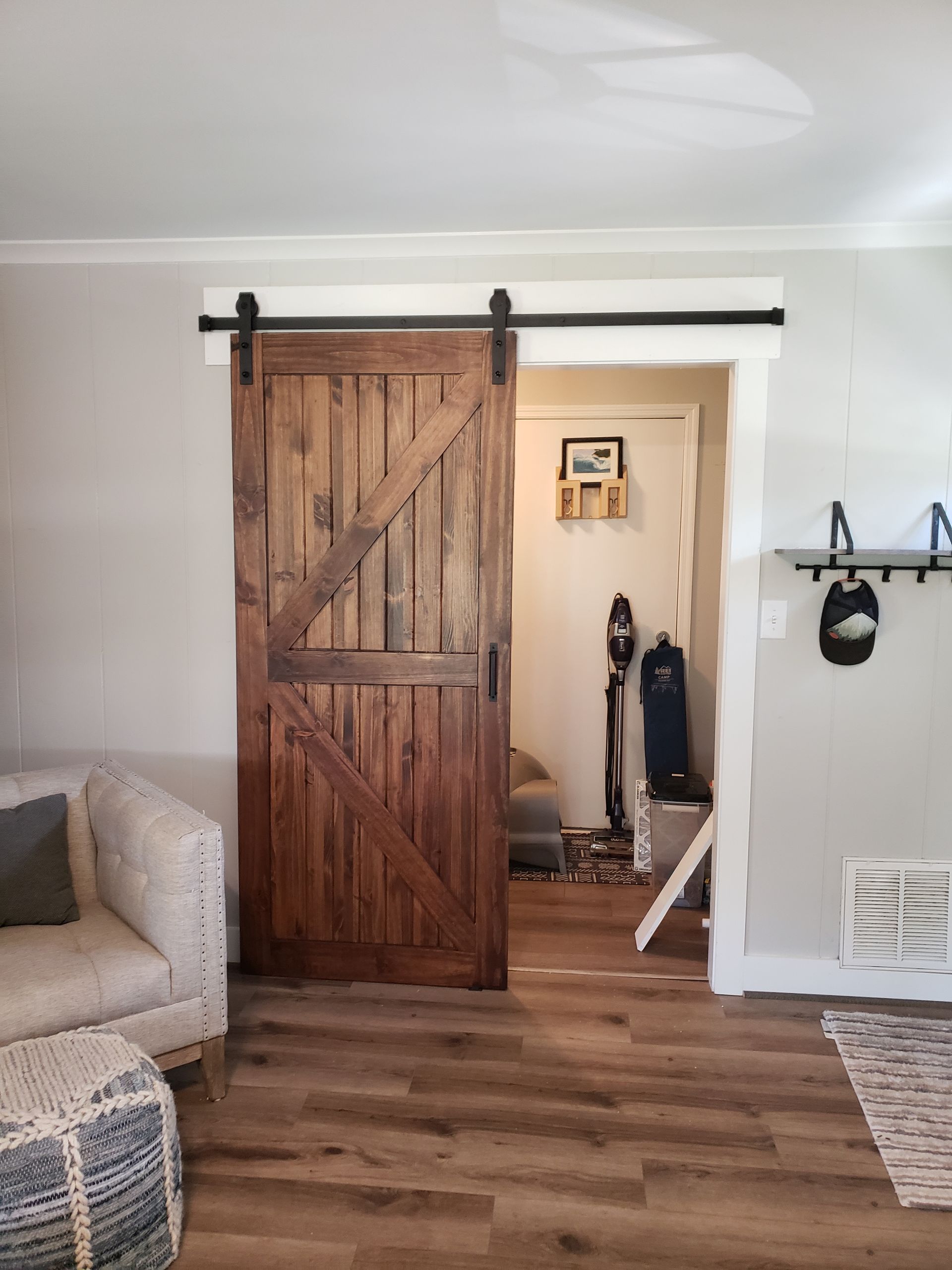 Wooden barn door, dark brown with a diagonal brace, on a black sliding track, leading to a small room.