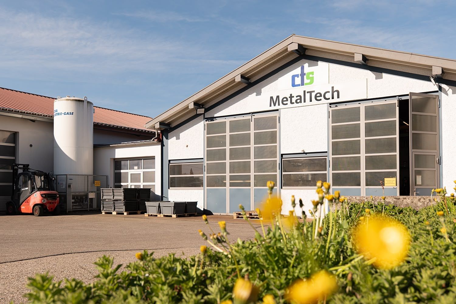 Das Industriegebäude von MetalTech mit weißer Fassade, großen Garagentoren und einem davor geparkten Gabelstapler.