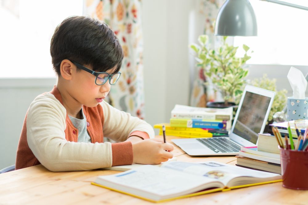 Boy Wearing Glasses Writes at a Desk With a Laptop and Open Book — RIP IT UP Reading in Central Coast, NSW