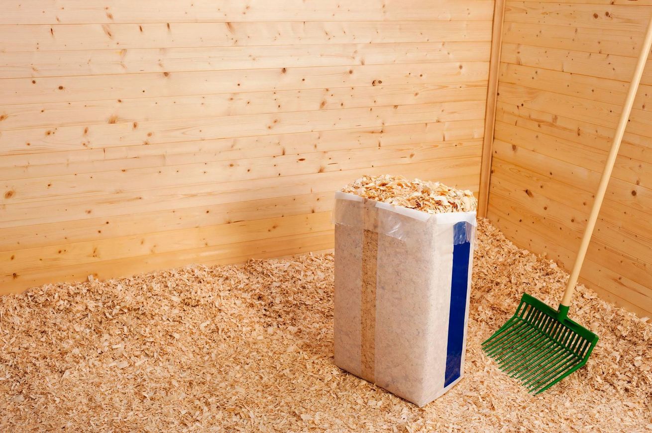 a bag of wood shavings and a green shovel in a wooden horse stall