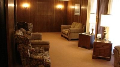 A dimly lit waiting room with wood paneling, patterned armchairs, and lamps.