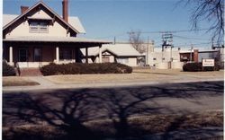A two-story house with a porch and a business sign. A tree's shadow is cast on the street in front.