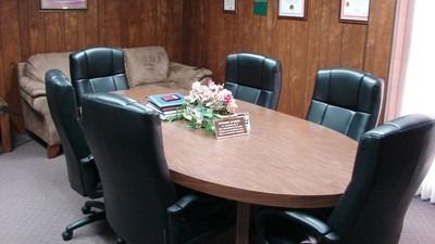 Conference room with oval table, six black leather chairs, sofa, wood-paneled walls, and documents.