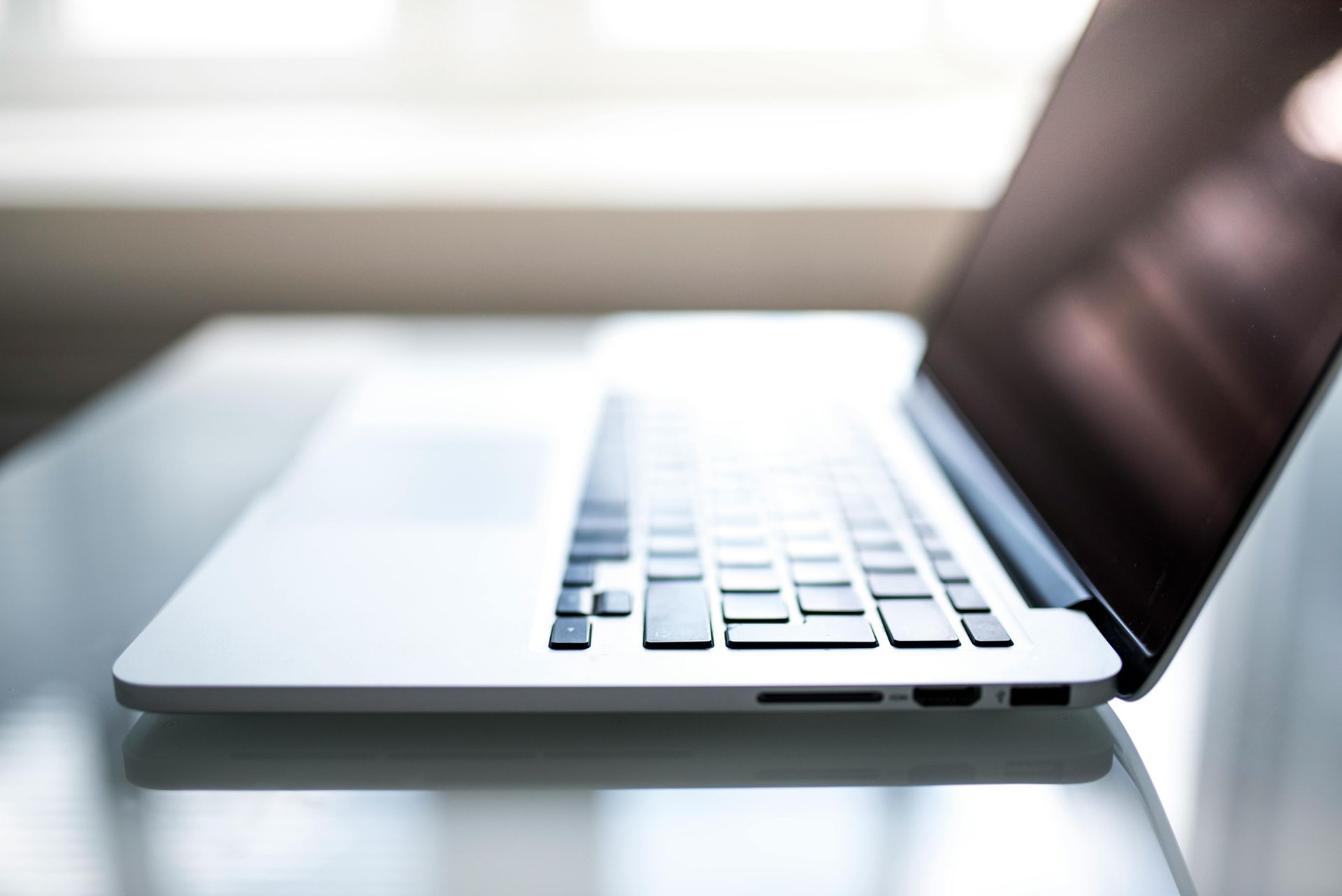 Silver laptop on a glass surface, screen open, keyboard visible, natural light.