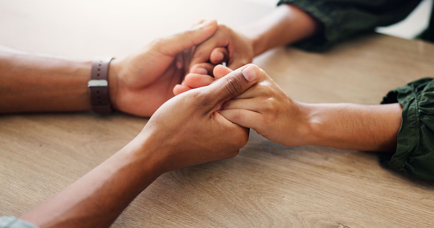 Hands clasped together on a wooden surface, offering comfort or support.