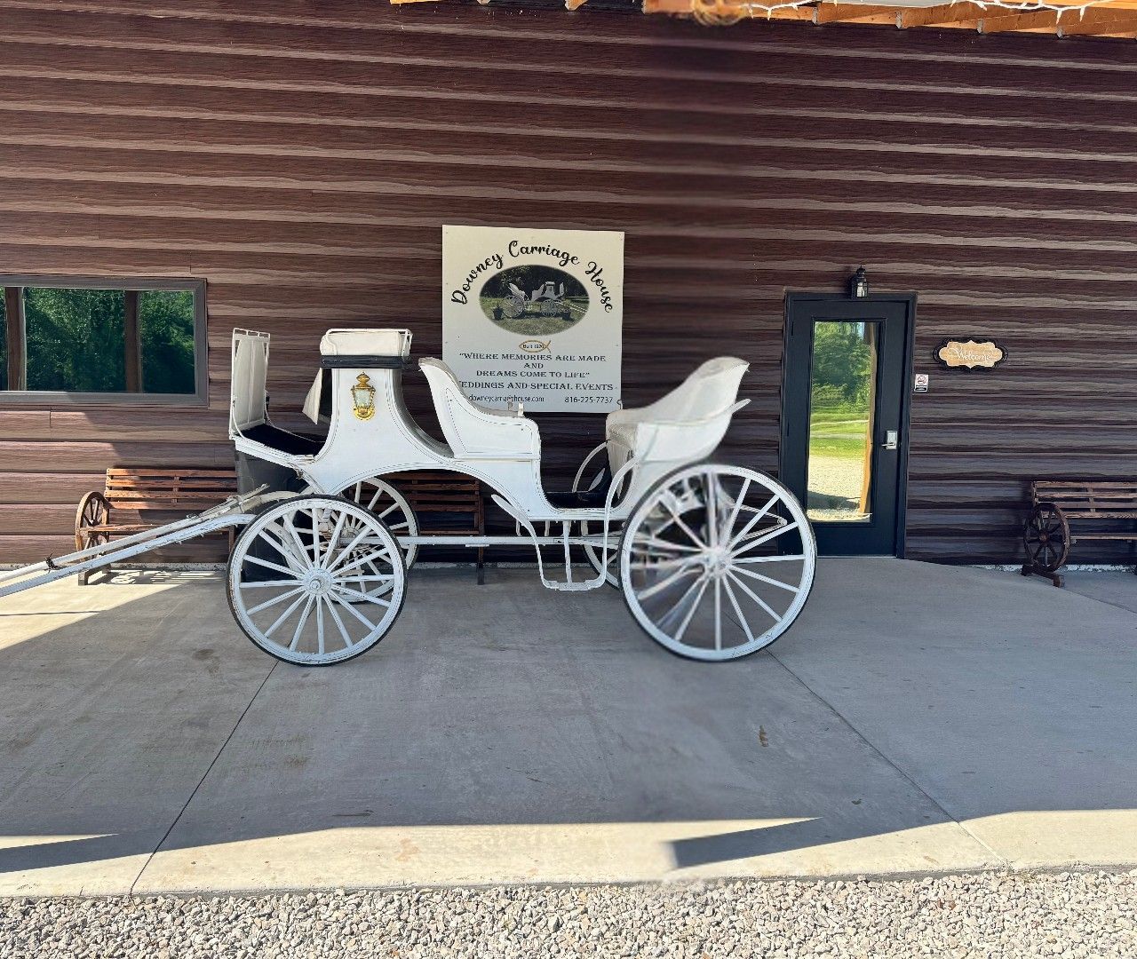 A white horse drawn carriage is parked in front of a wooden building. A white horse drawn carriage is parked in front of a wooden building.