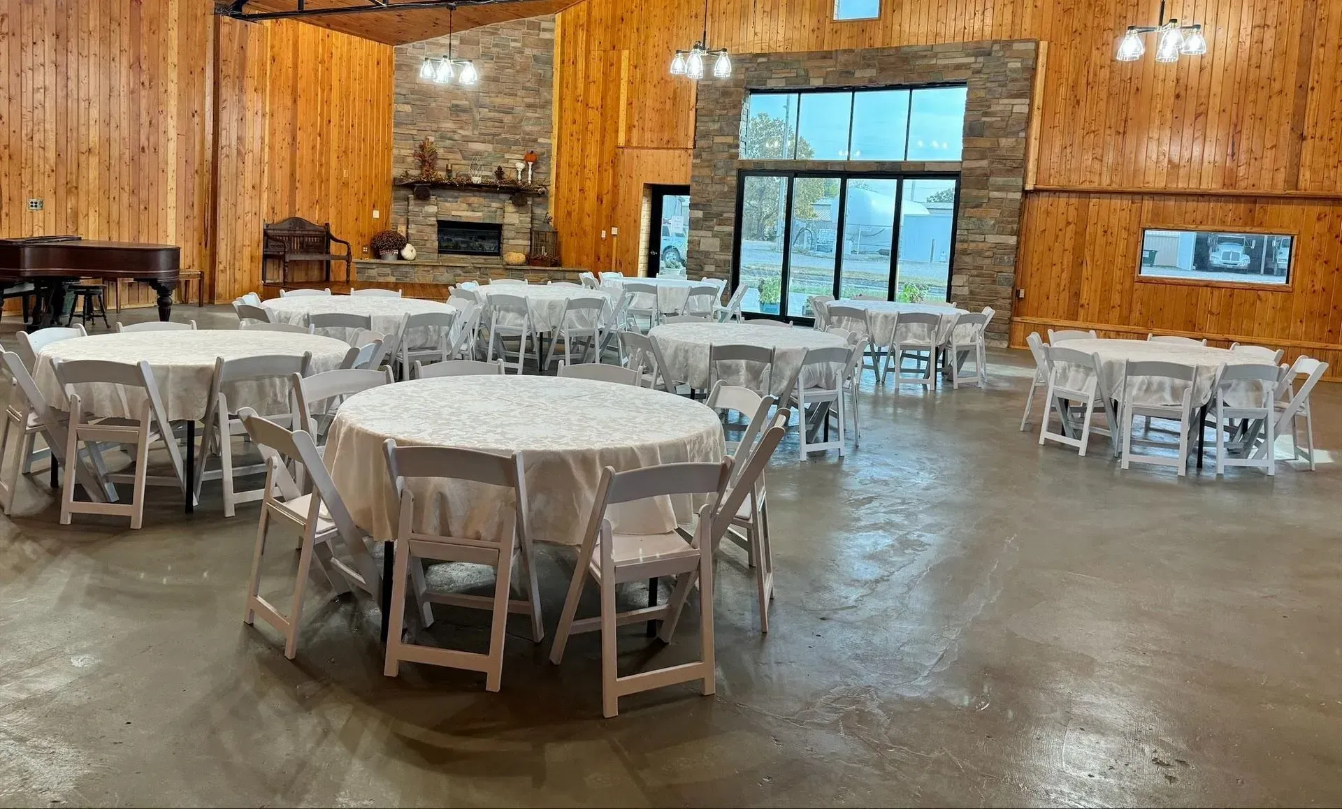Event hall with round tables set with white linens and chairs. Wooden walls and a stone fireplace.